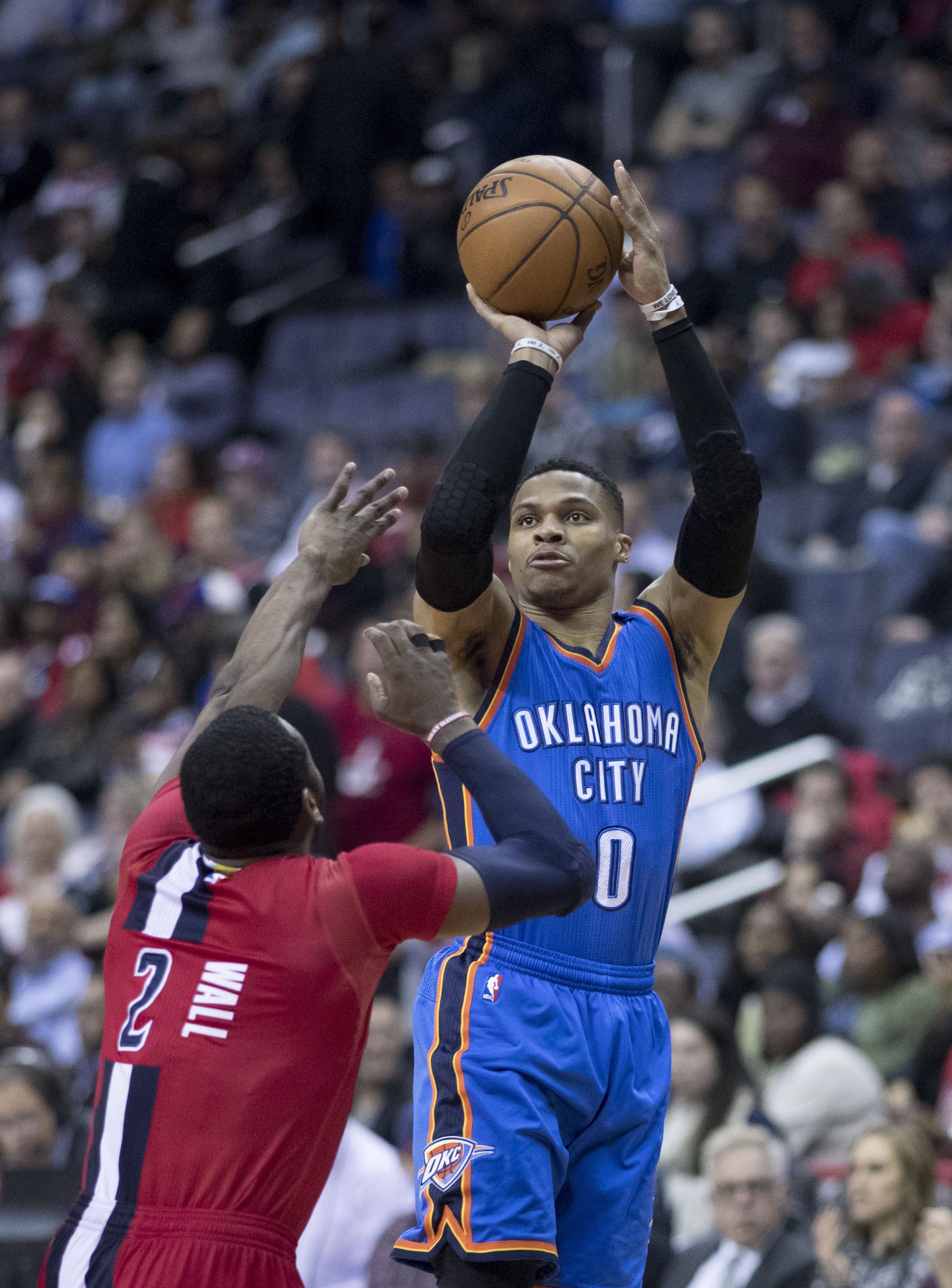 Basketball player in blue Thunder jersey number 0 shooting over a red-jersey defender.