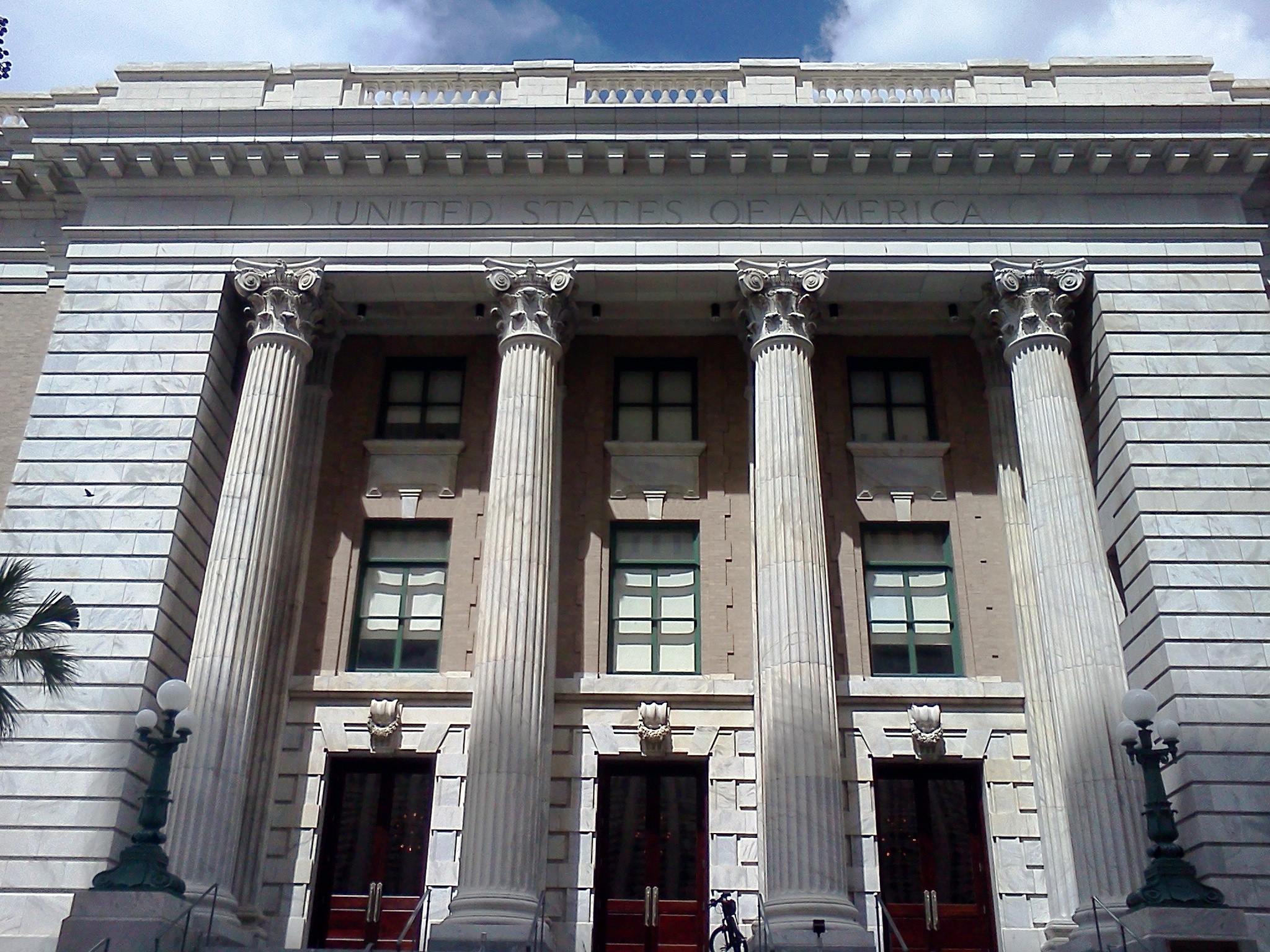 Neoclassical federal courthouse exterior with tall columns and red entry doors.