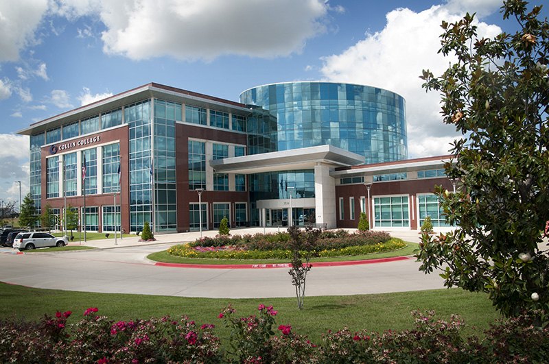Modern multi-story college building with glass curtain walls and a landscaped circular drive.