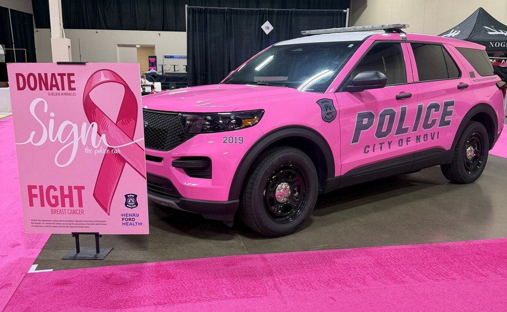 Pink police SUV marked 'City of Novi' parked next to a breast cancer awareness donation sign.