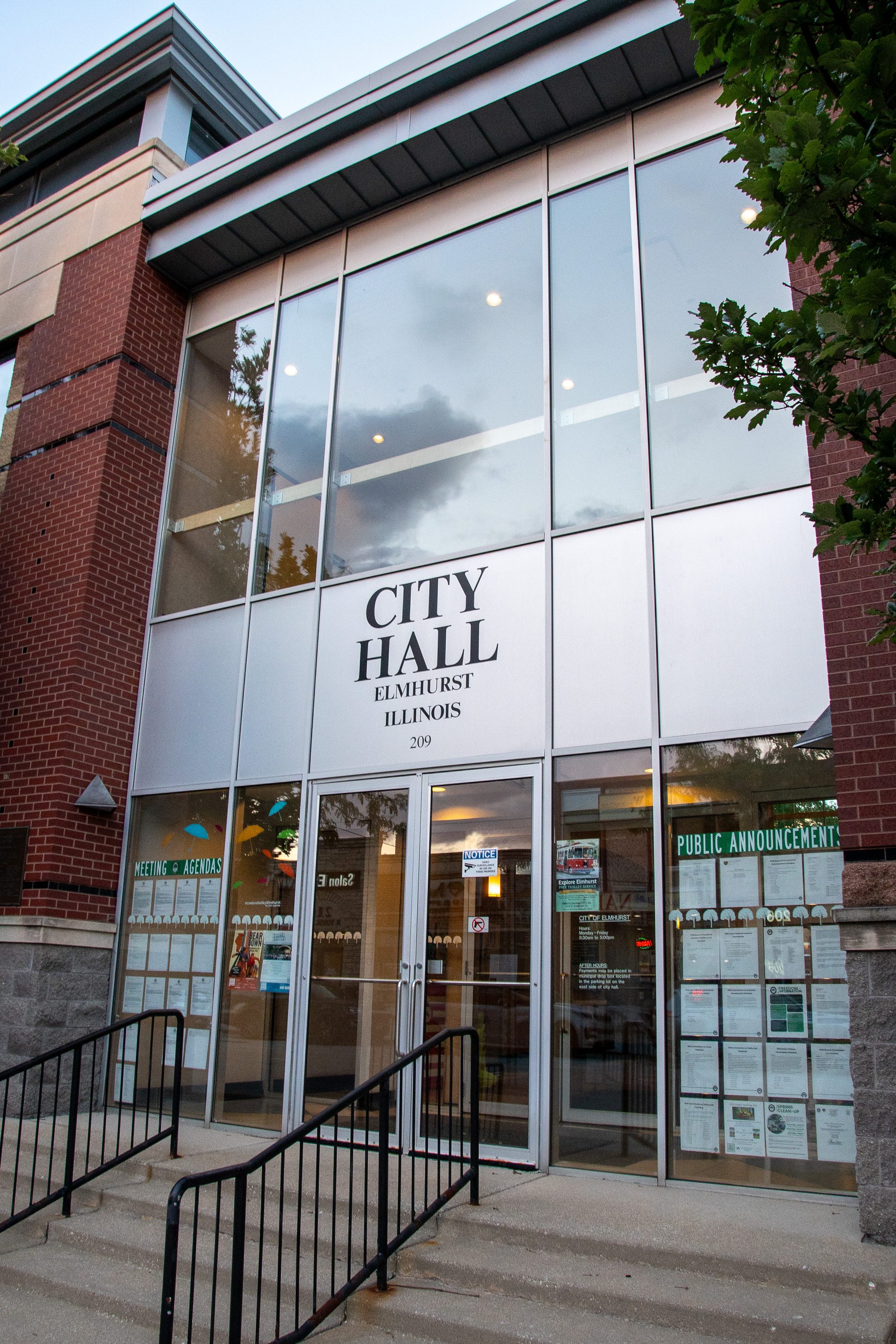 Glass-and-brick entrance of a city hall building with signage above the doors.