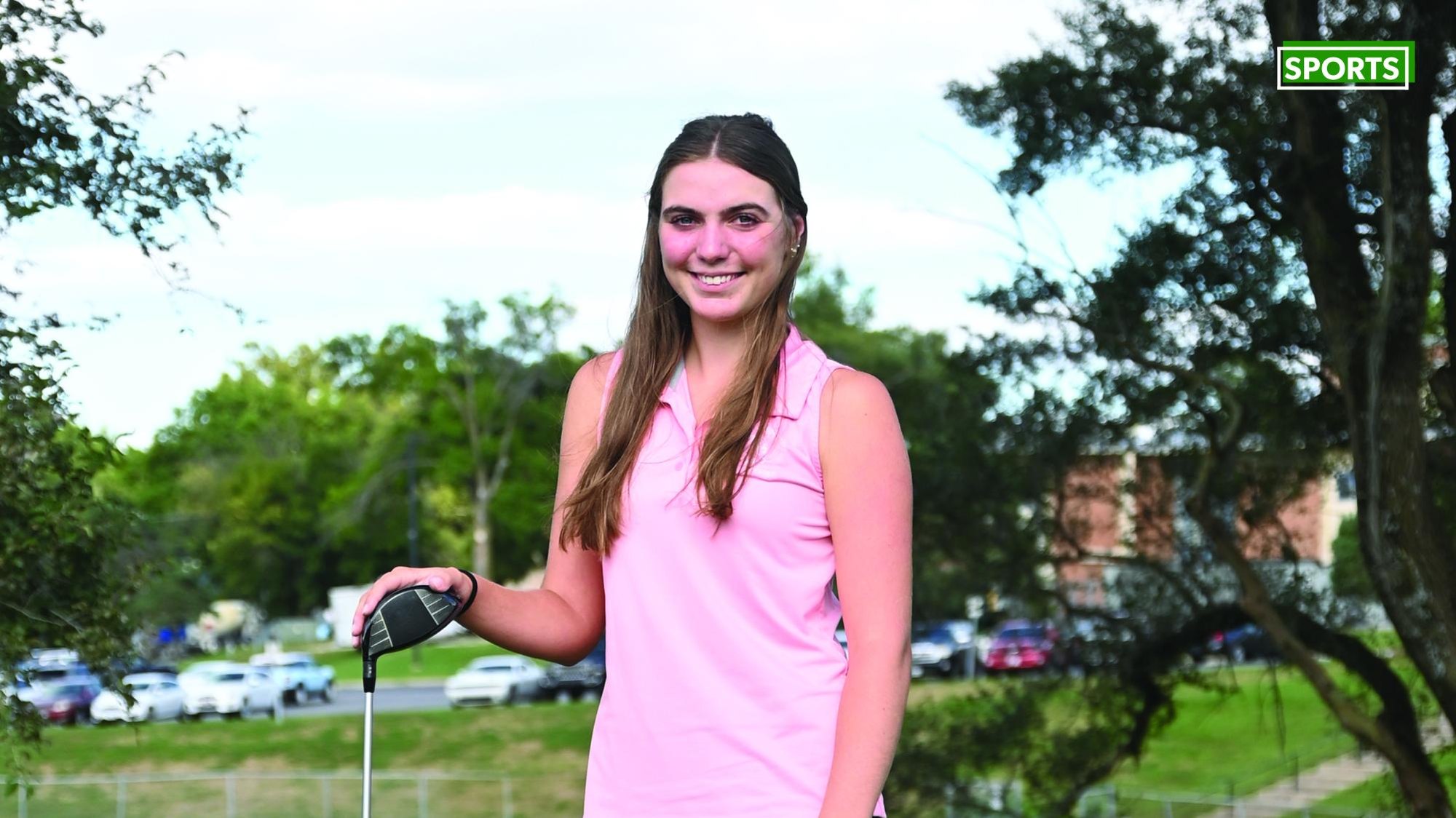 Young woman in a pink polo shirt holding a golf club outdoors.