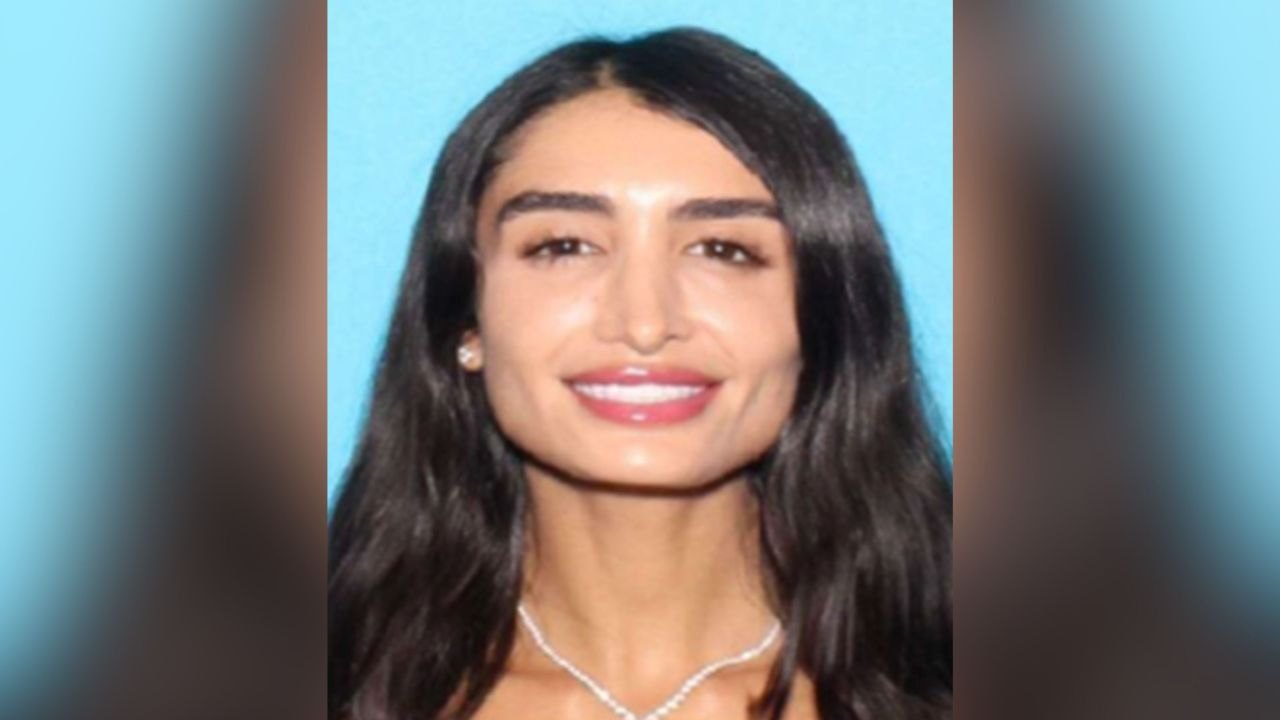 Woman with long dark wavy hair and pearl necklace in an official identification photo.
