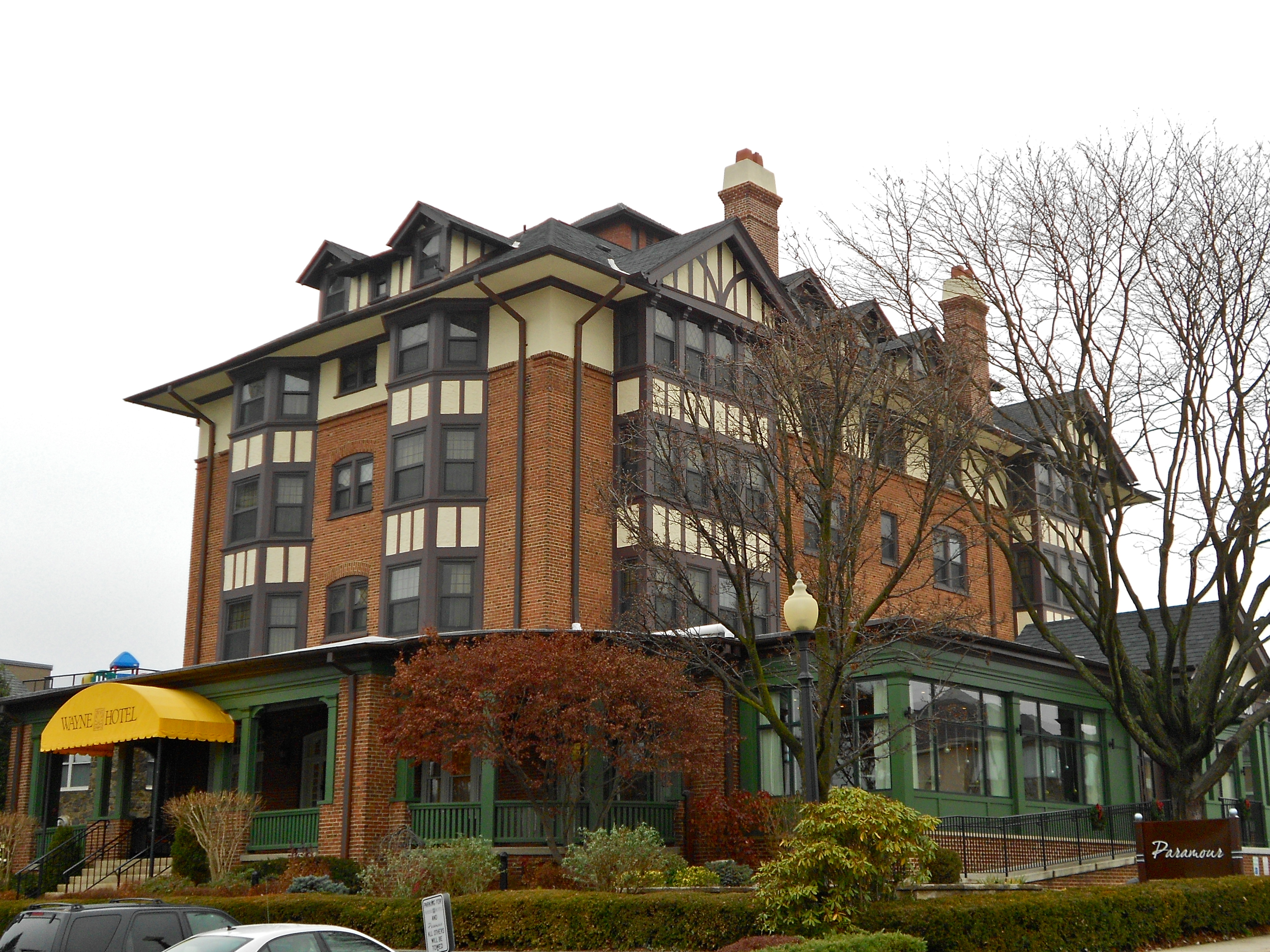 Wide view of a large brick Tudor Revival hotel building with green trim and bare trees.