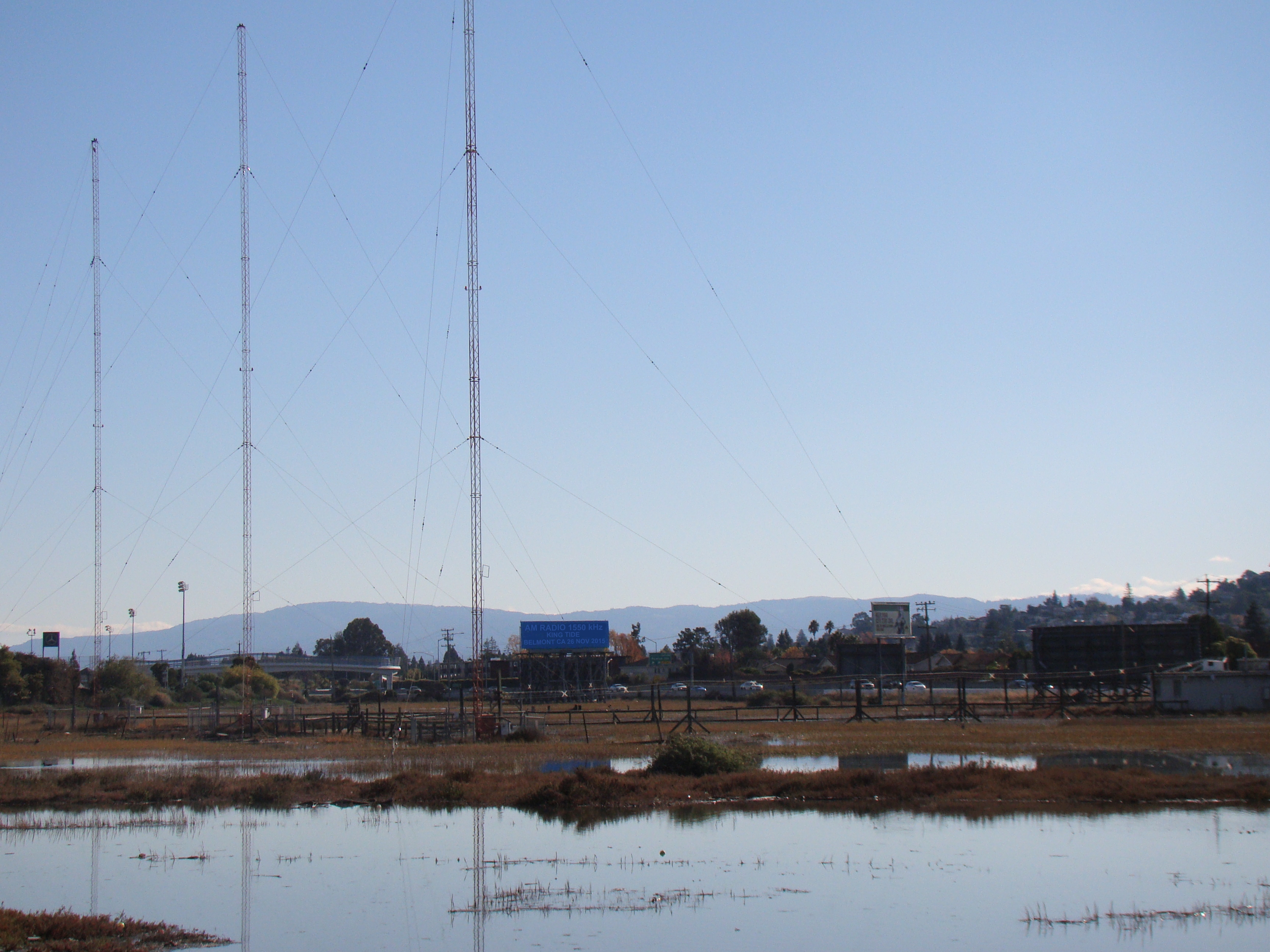 Radio towers surrounded by standing floodwater near San Francisco Bay during a king tide.