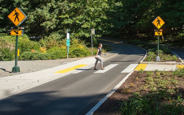 Woman walking through a marked crosswalk with flashing beacon warning signs on both sides.