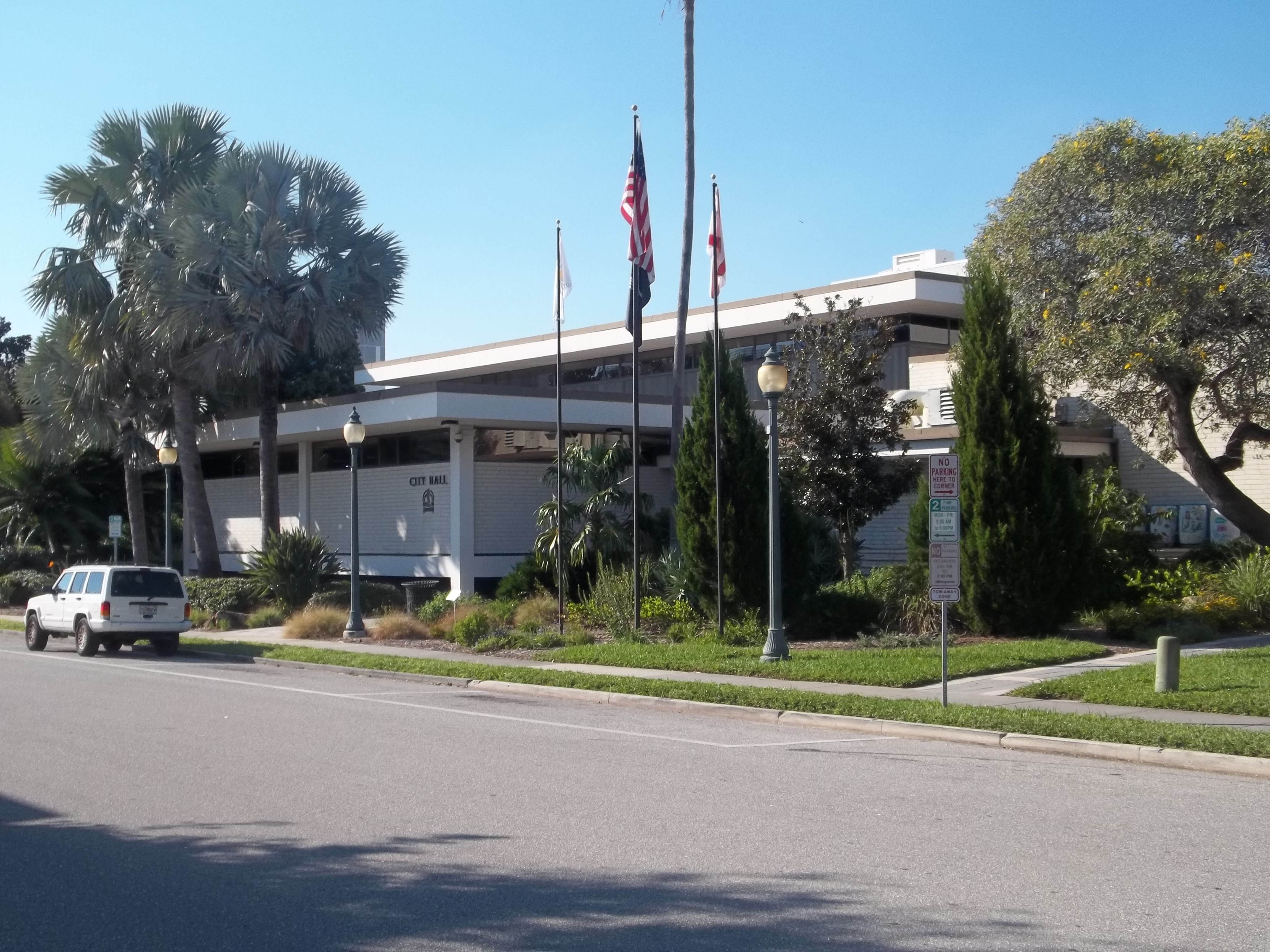 Low-rise Sarasota City Hall with flagpoles and palm trees on a sunny day.