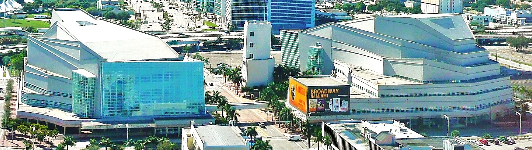 Aerial view of a large white performing arts complex with palm trees and a Broadway billboard.