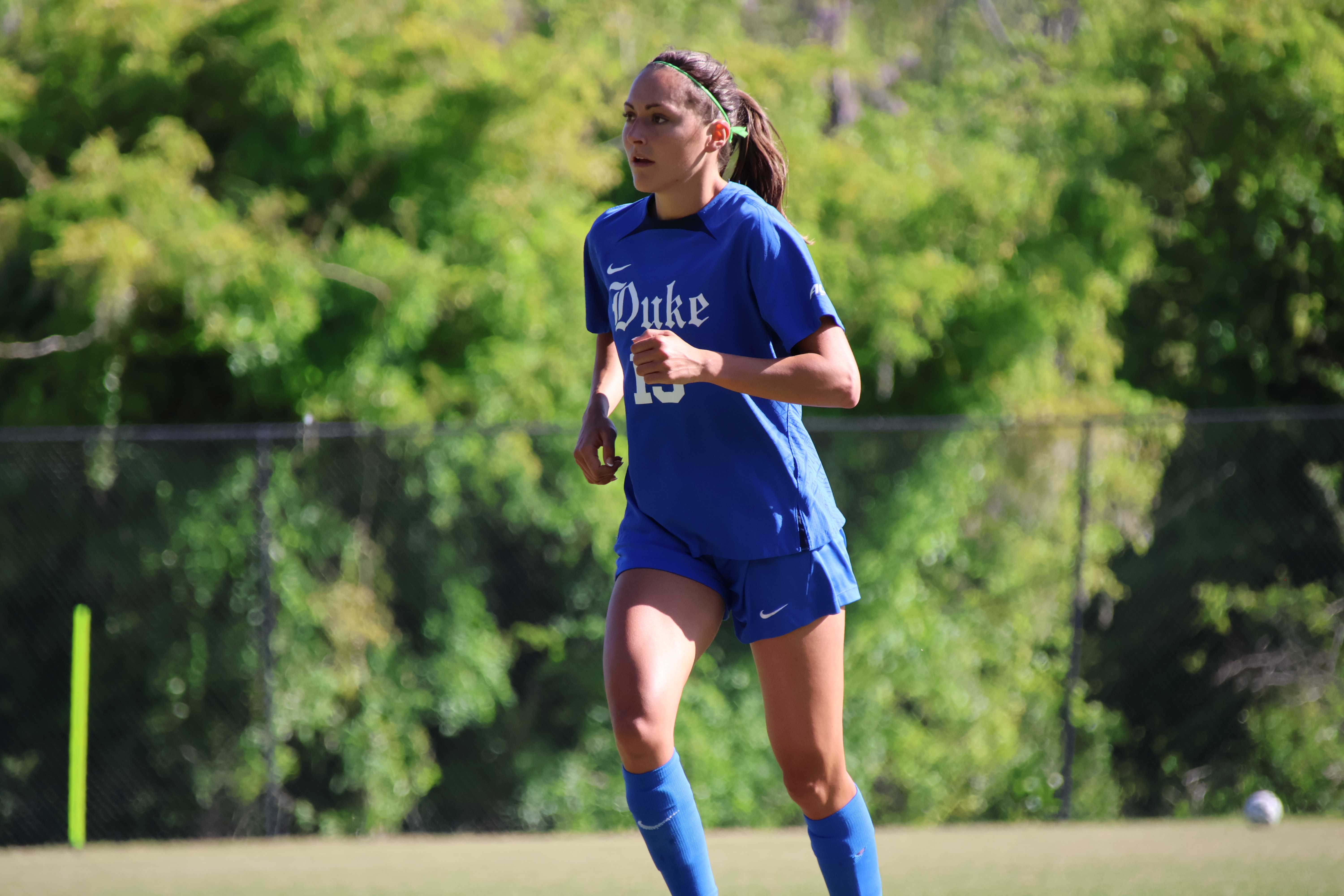 A female soccer player in a blue Duke uniform running on a grass field.