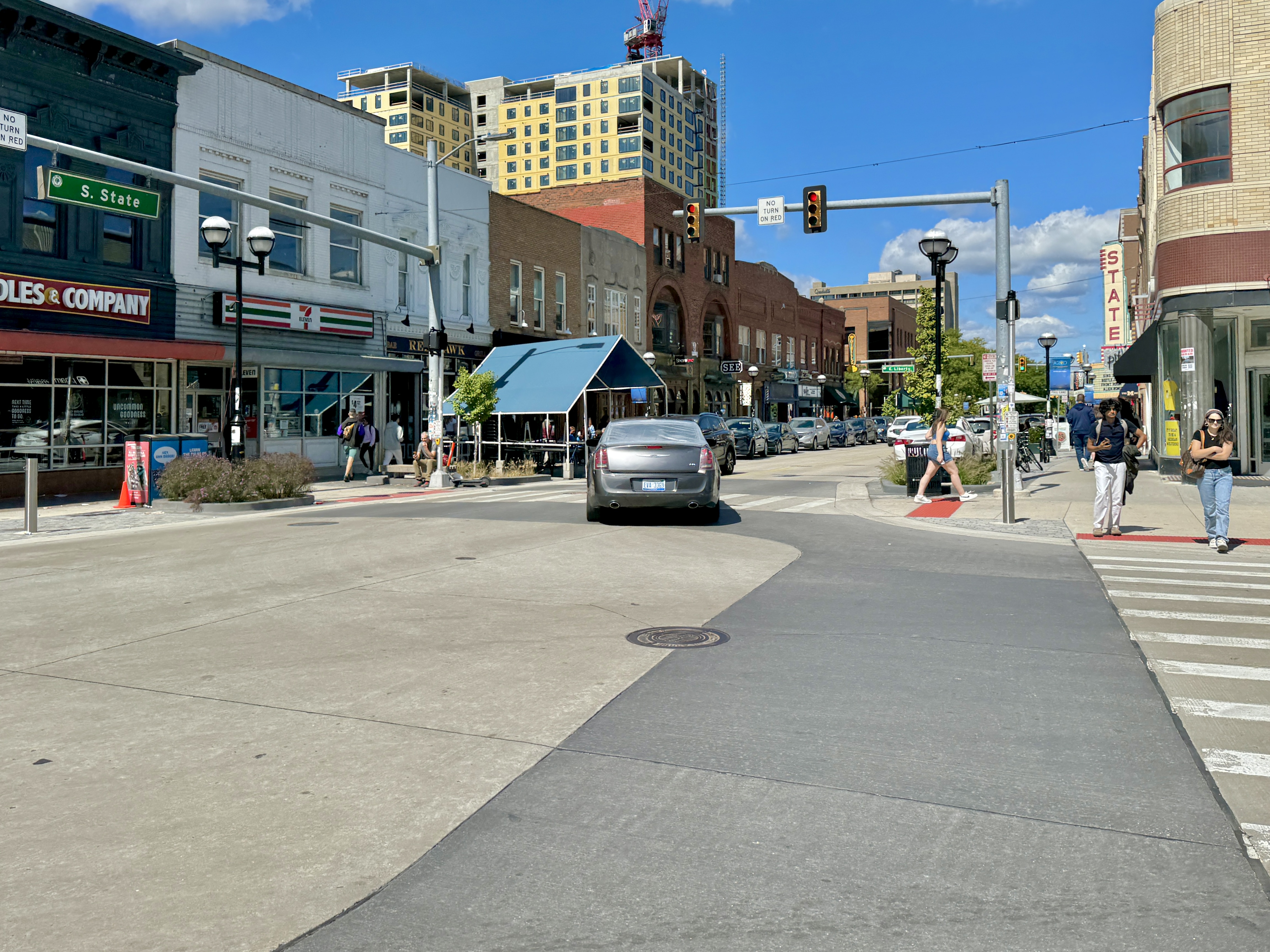 A downtown street with historic brick commercial buildings, a car at an intersection, and pedestrians on the sidewalk.