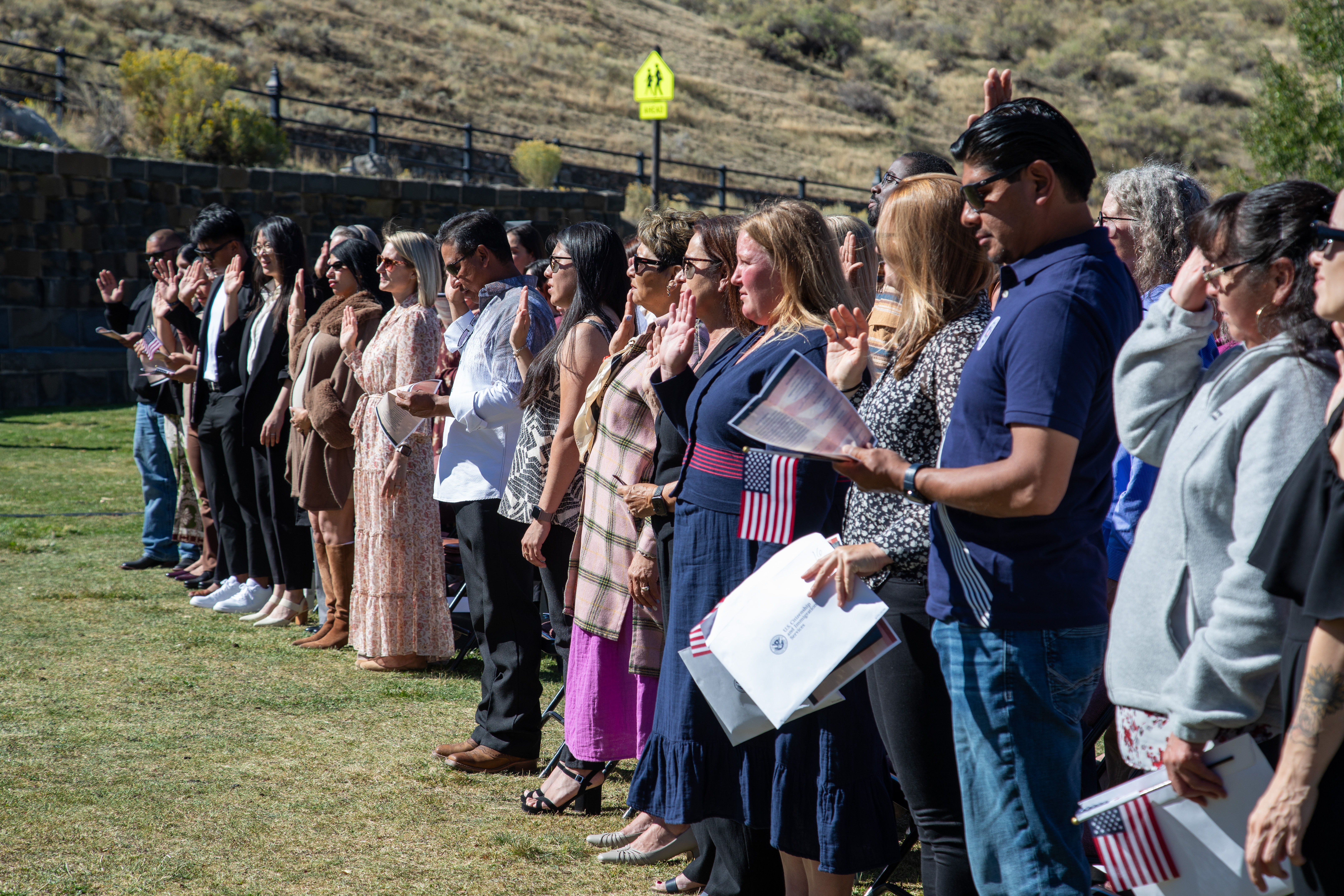 A large group of people raising their right hands outdoors at a naturalization ceremony.