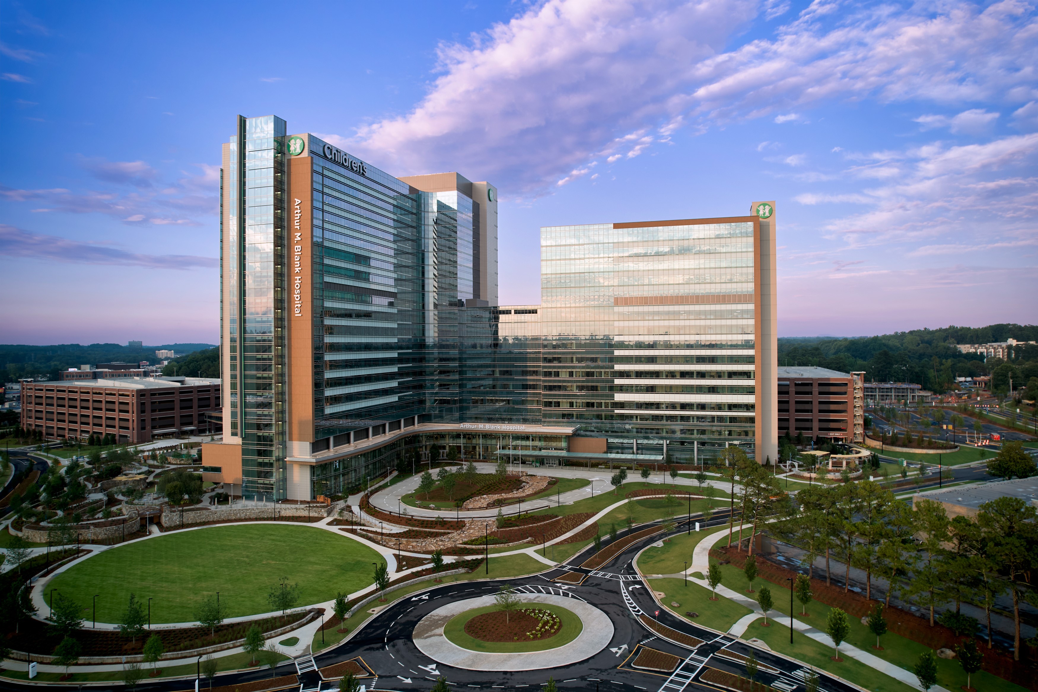 Aerial dusk view of a large modern glass-and-steel hospital complex with a circular driveway.