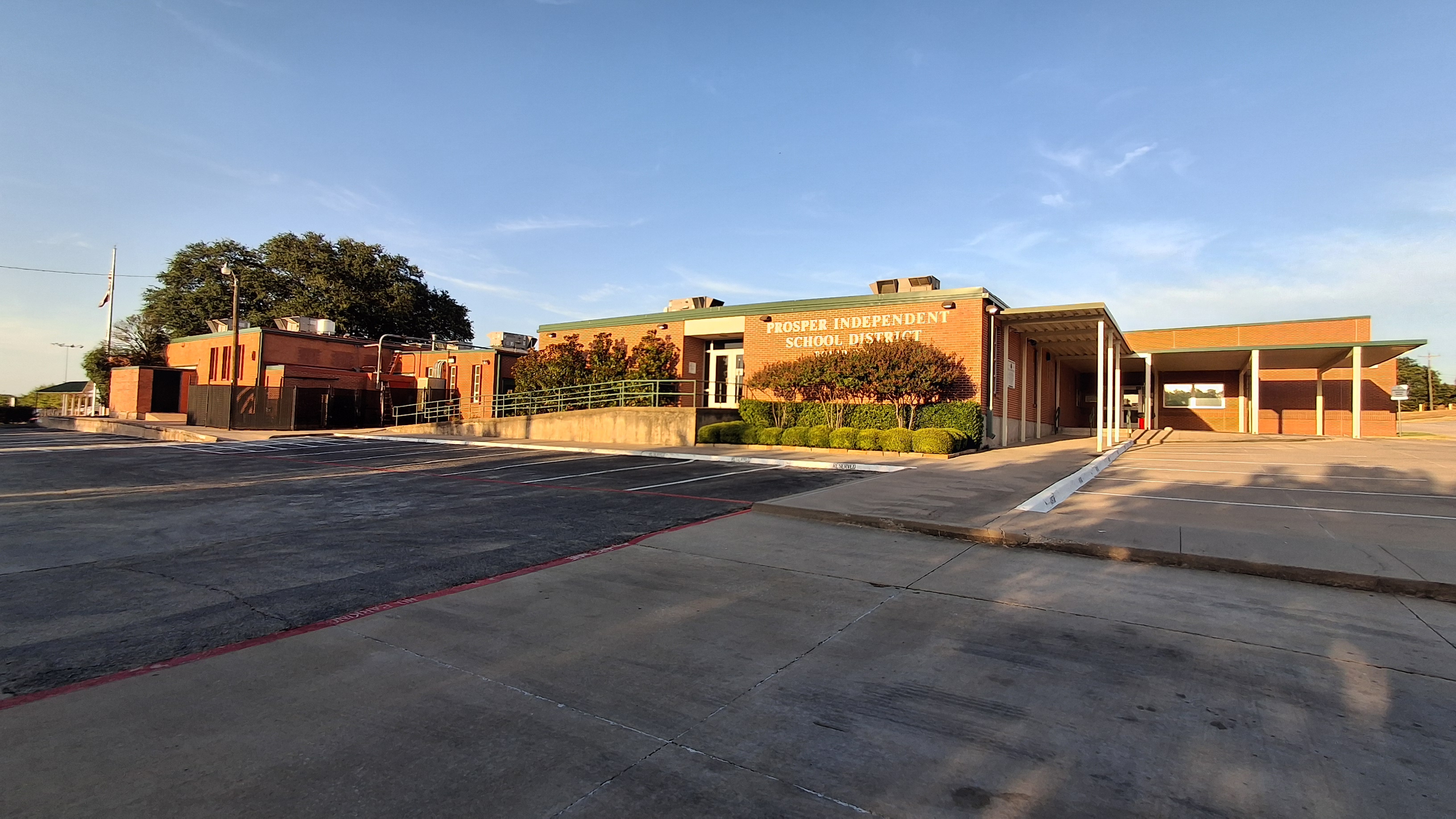 Low-rise brick administration building with a green-trimmed entrance canopy and parking lot.