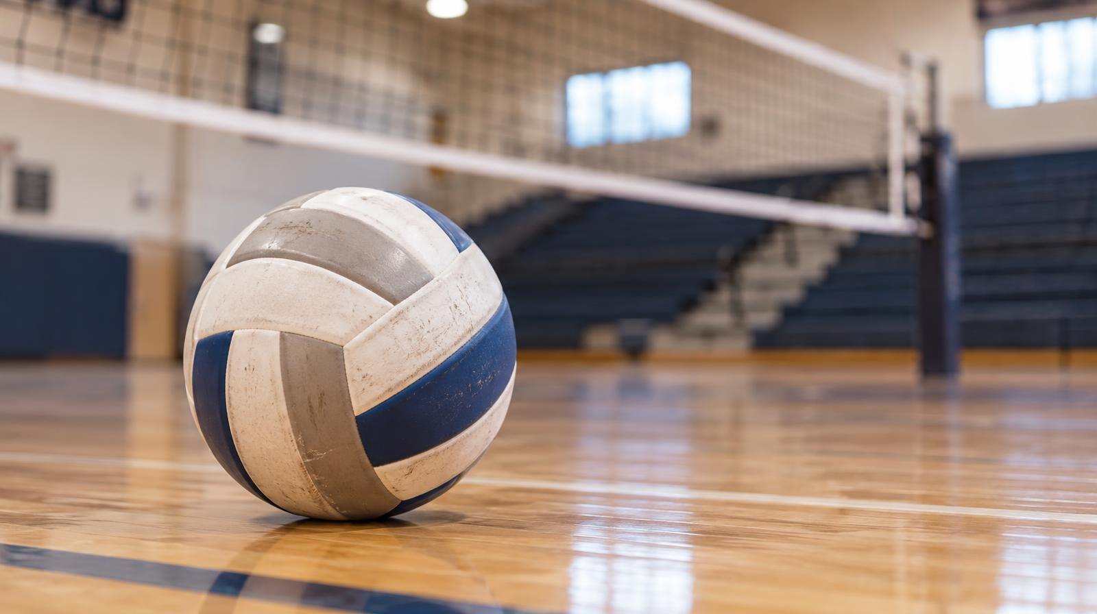 A volleyball resting on a hardwood gymnasium floor near a net.