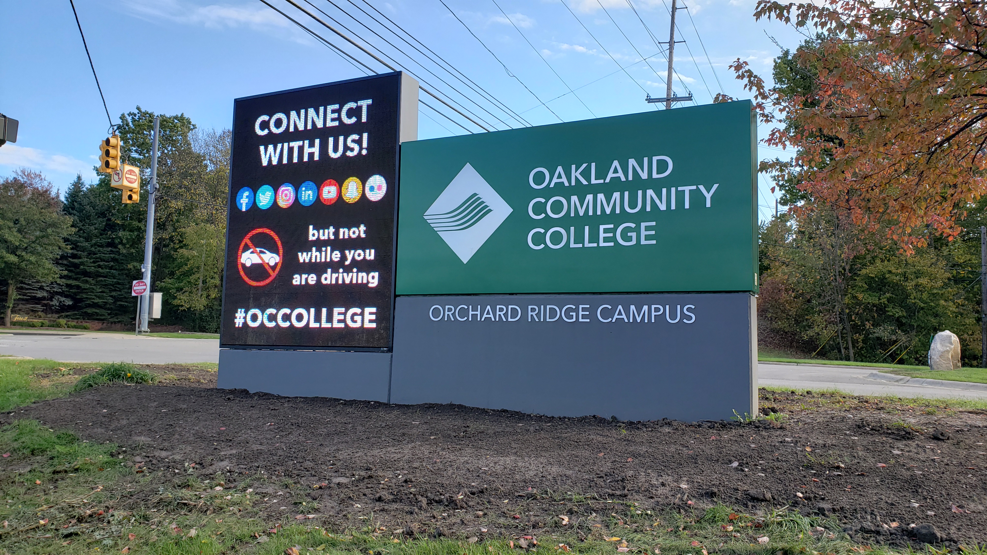 Monument sign for a college campus along a tree-lined road in autumn.
