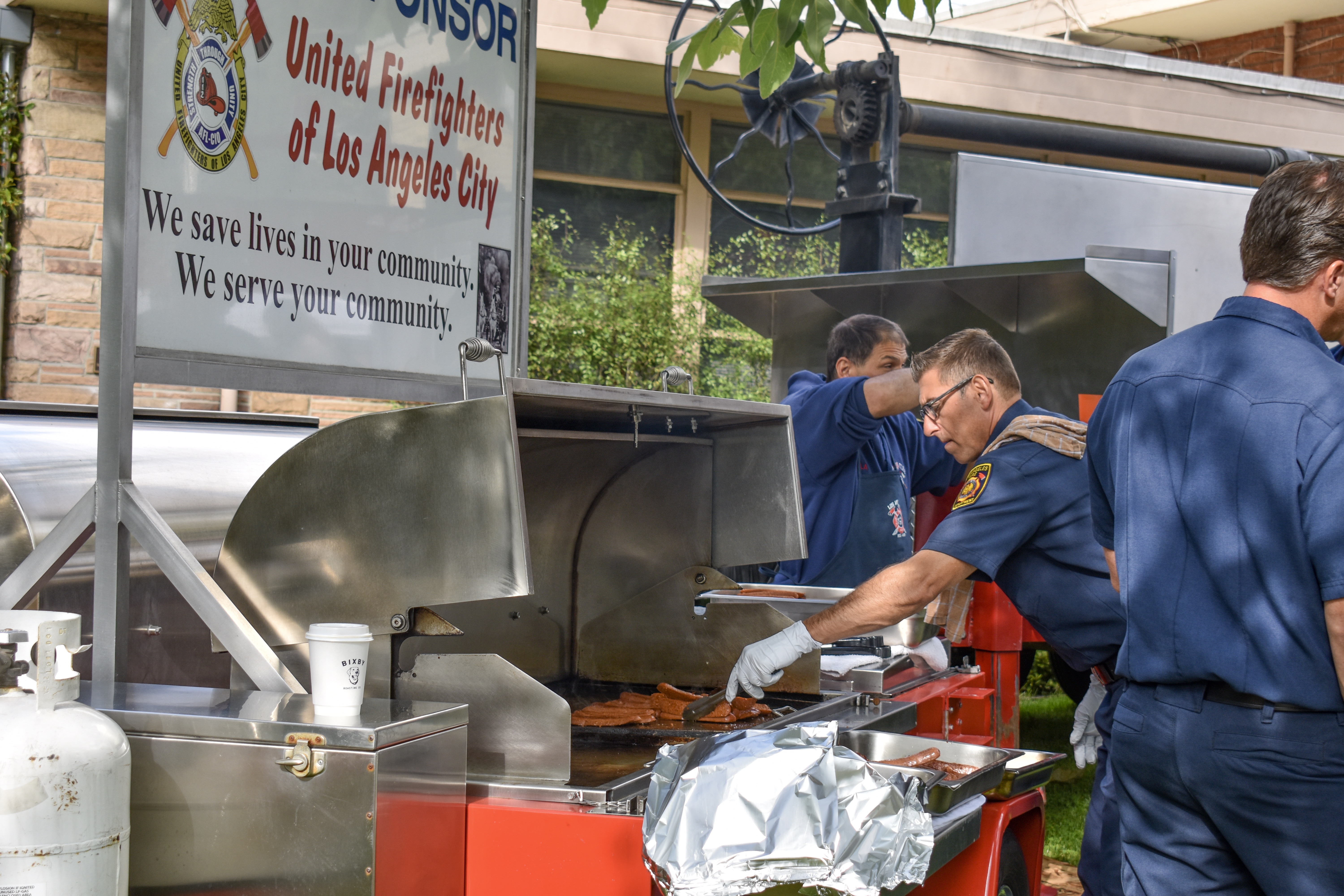 Firefighters in LAFD uniforms cooking at an outdoor grill at a community pancake breakfast