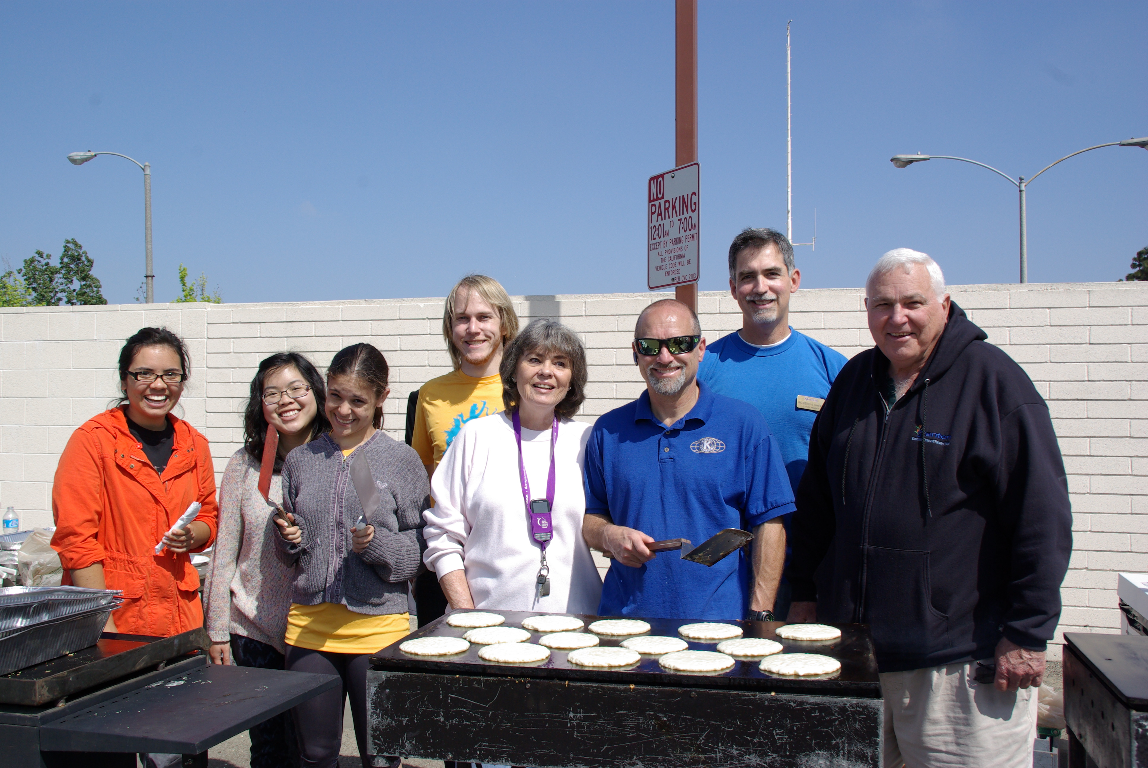 Volunteers stand behind a large outdoor griddle cooking pancakes at a community breakfast.