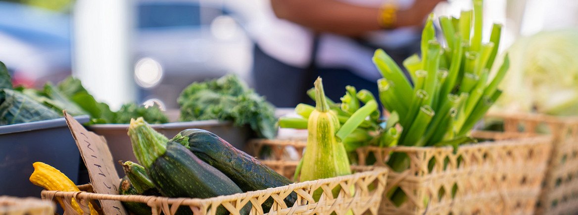 Woven baskets of zucchini, squash, kale, and greens on a farmers market table.