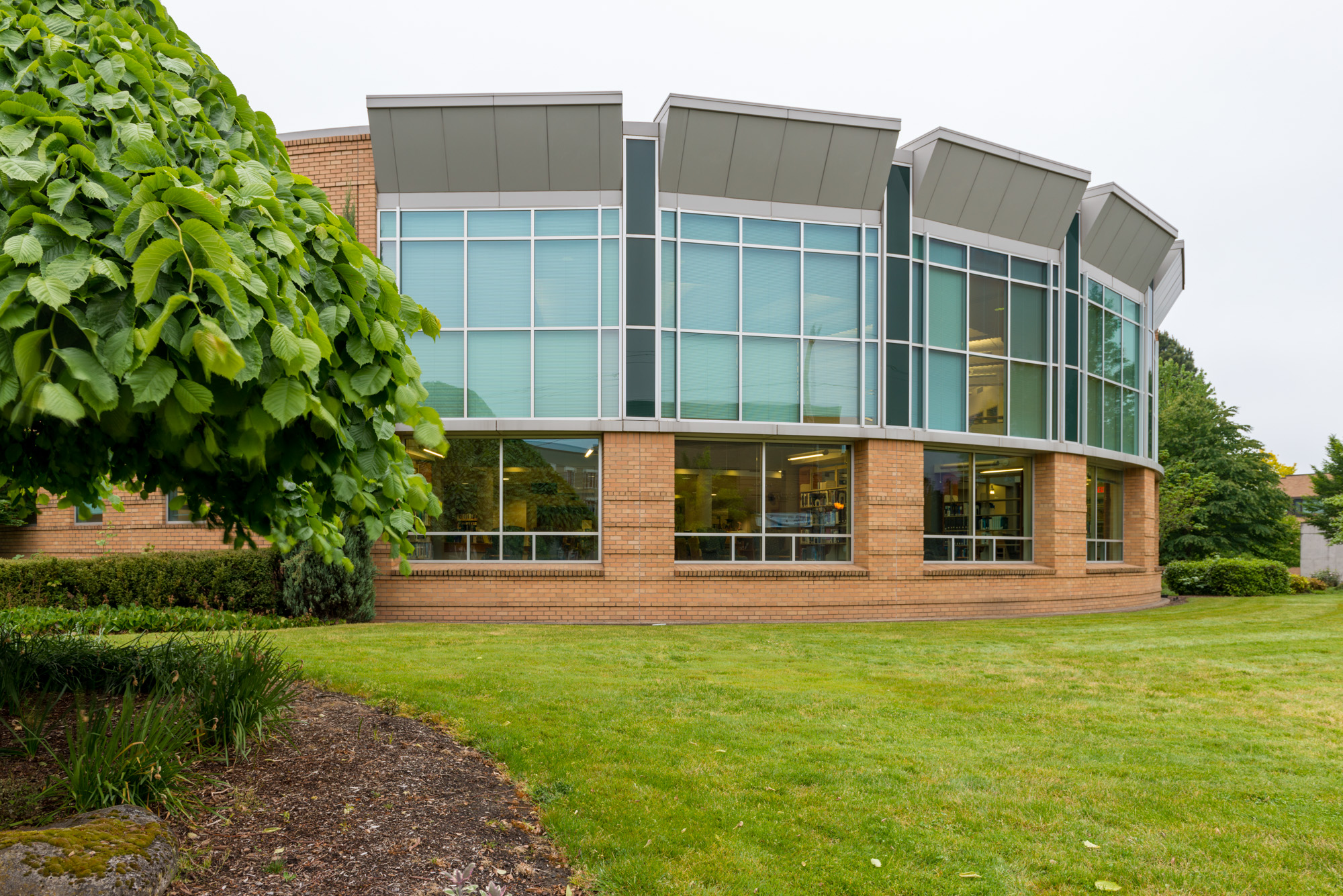 Modern two-story college building with curved glass windows and brick facade on a green campus.