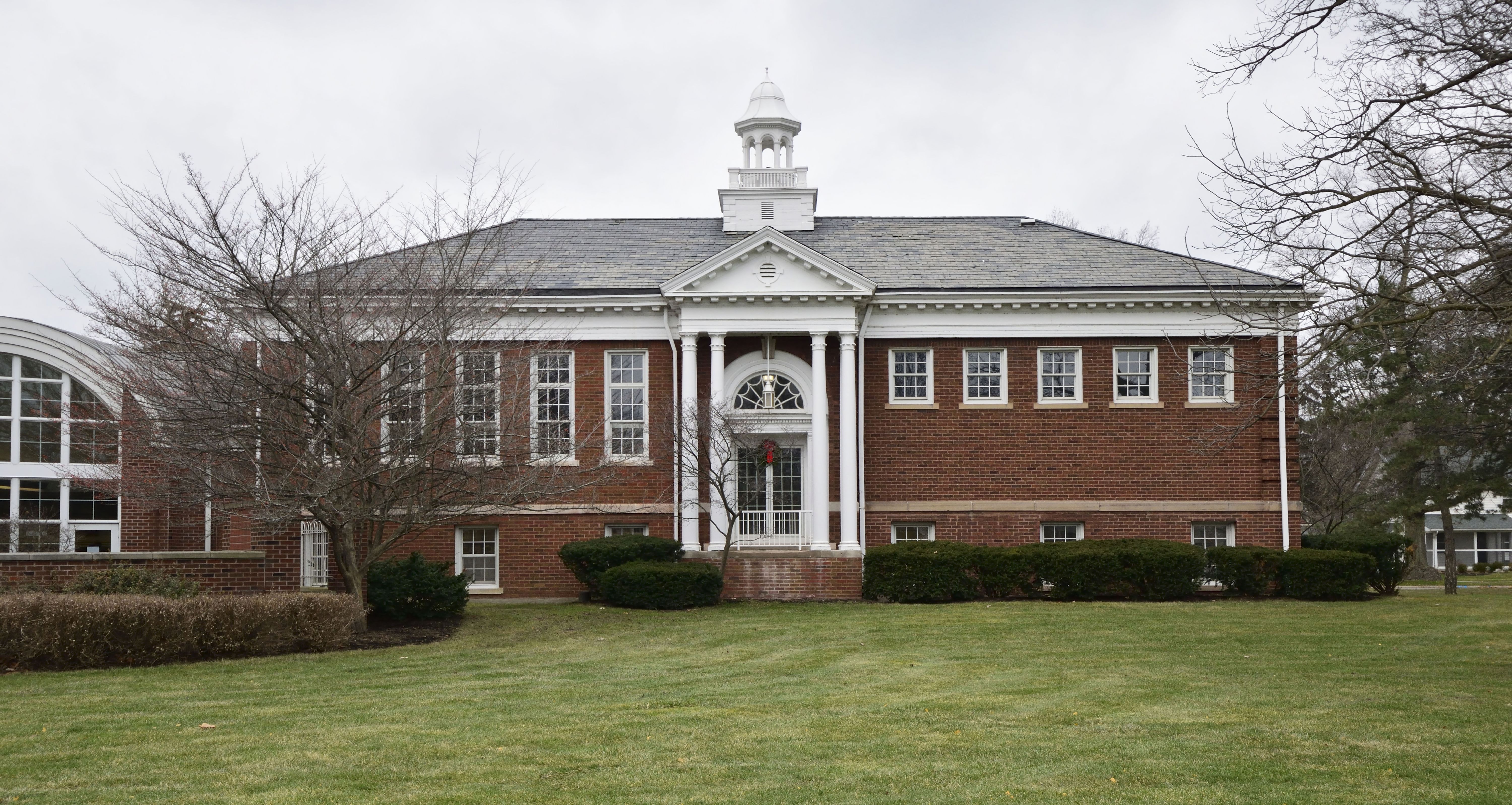 Two-story red brick library building with white columns and a cupola on an overcast day.