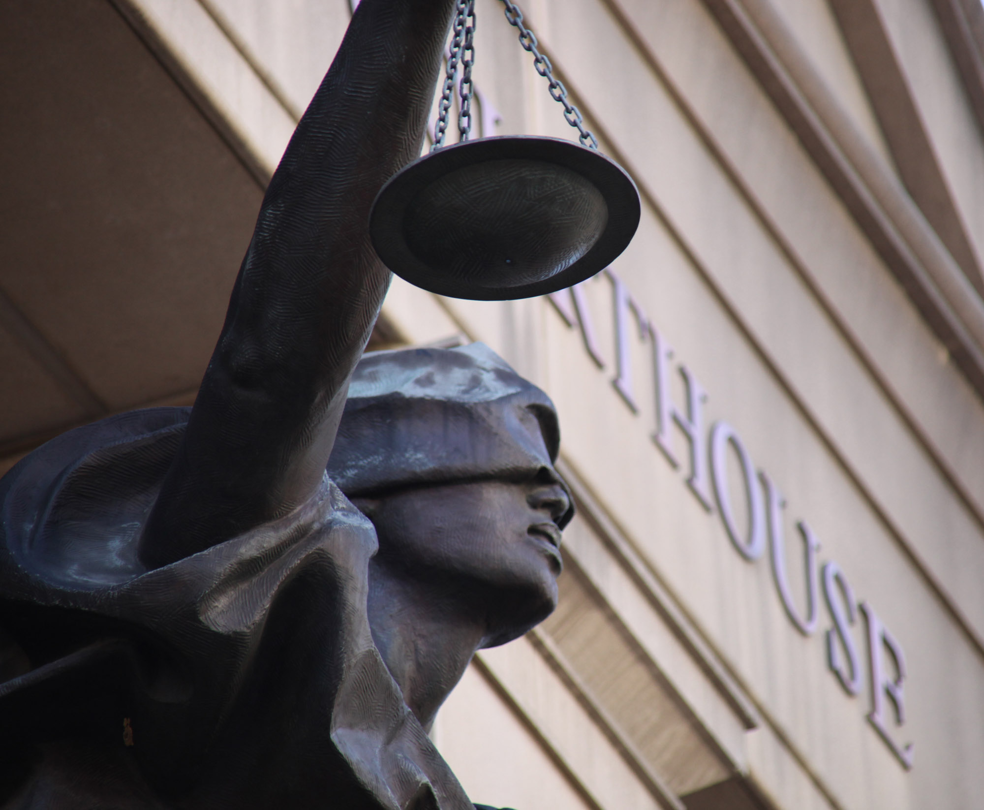 Bronze Blind Justice statue holding scales on the facade of a federal courthouse.