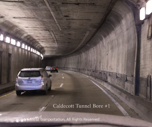 A car drives through the curved, tube-shaped interior of Caldecott Tunnel's Bore 1 on eastbound SR-24, with rows of overhead lights lining the walls.