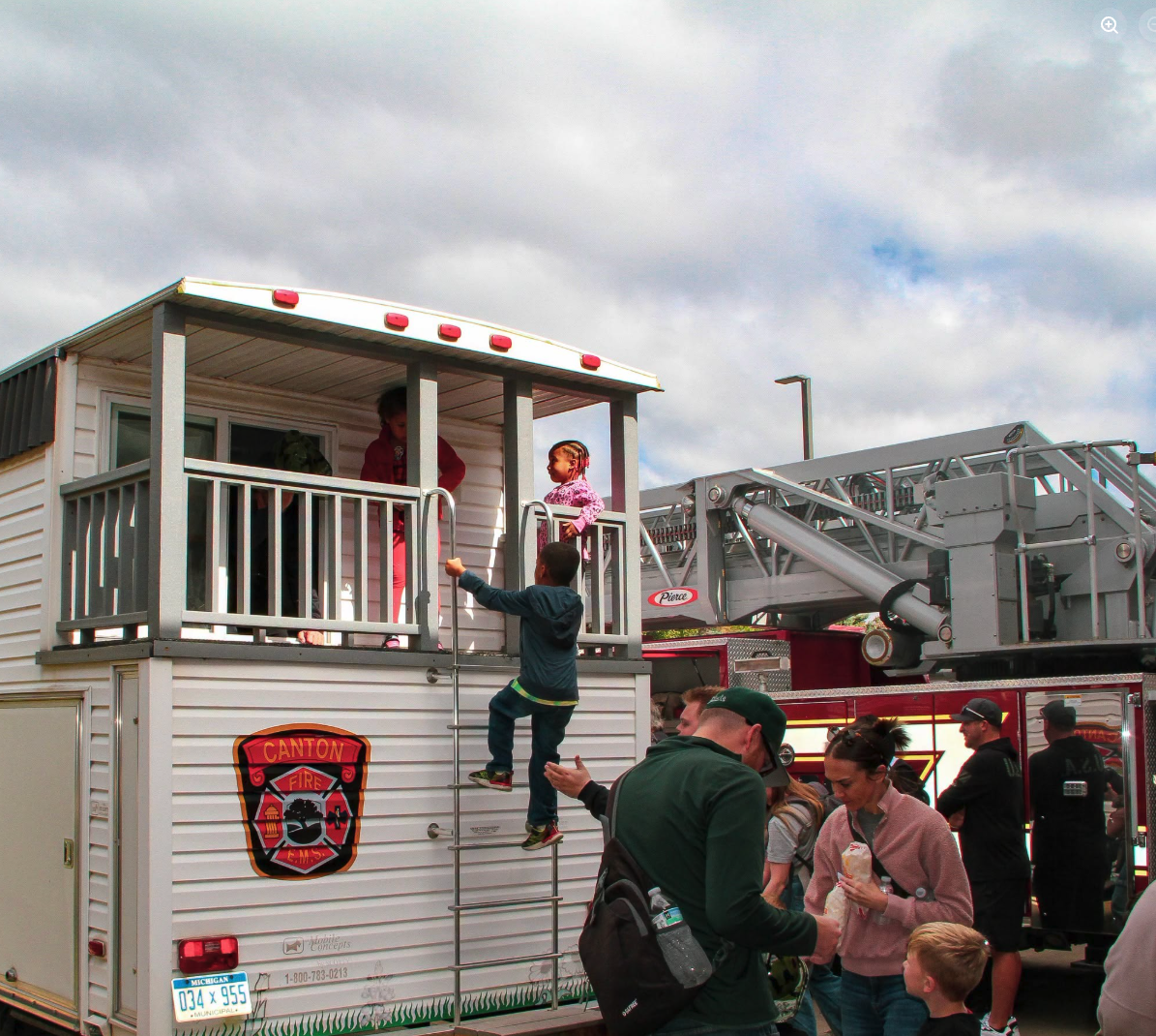 Children explore a Canton fire safety-house trailer while families gather beside a red ladder truck.