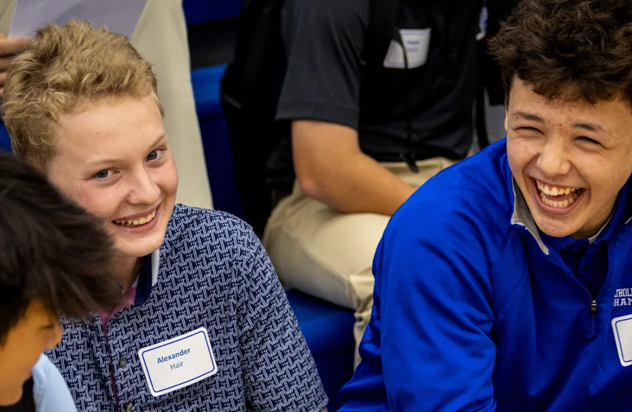 Two Catholic Central freshmen laughing together at freshman orientation, wearing name tags.