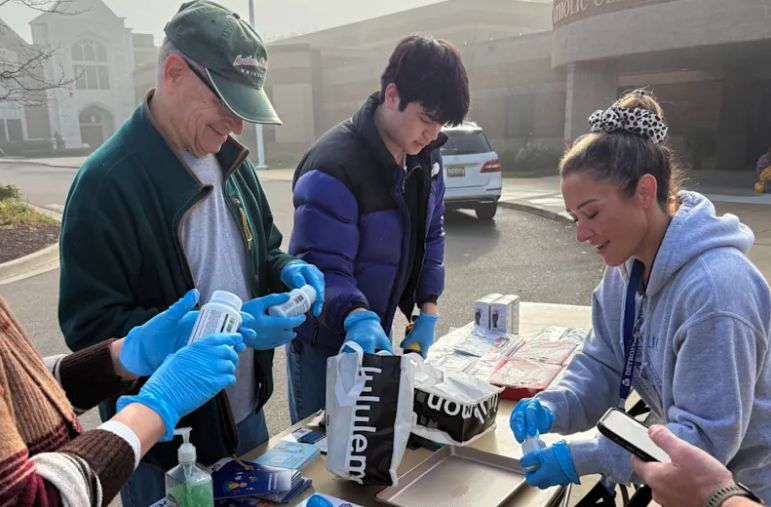 Volunteers wearing blue gloves sort medication containers on a table outside Catholic Central.