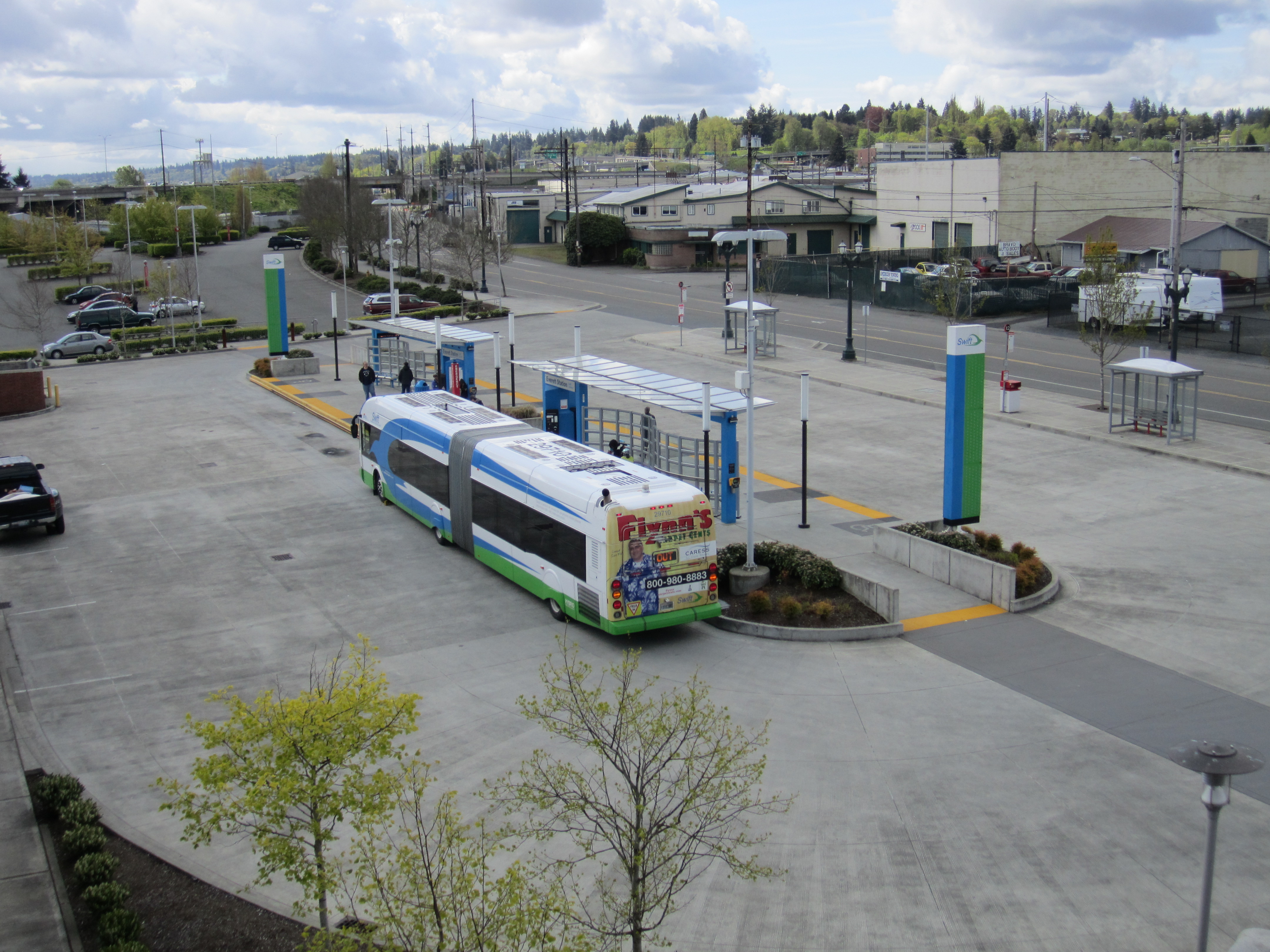 An articulated Swift bus at a covered transit center with teal columns and a concrete plaza.
