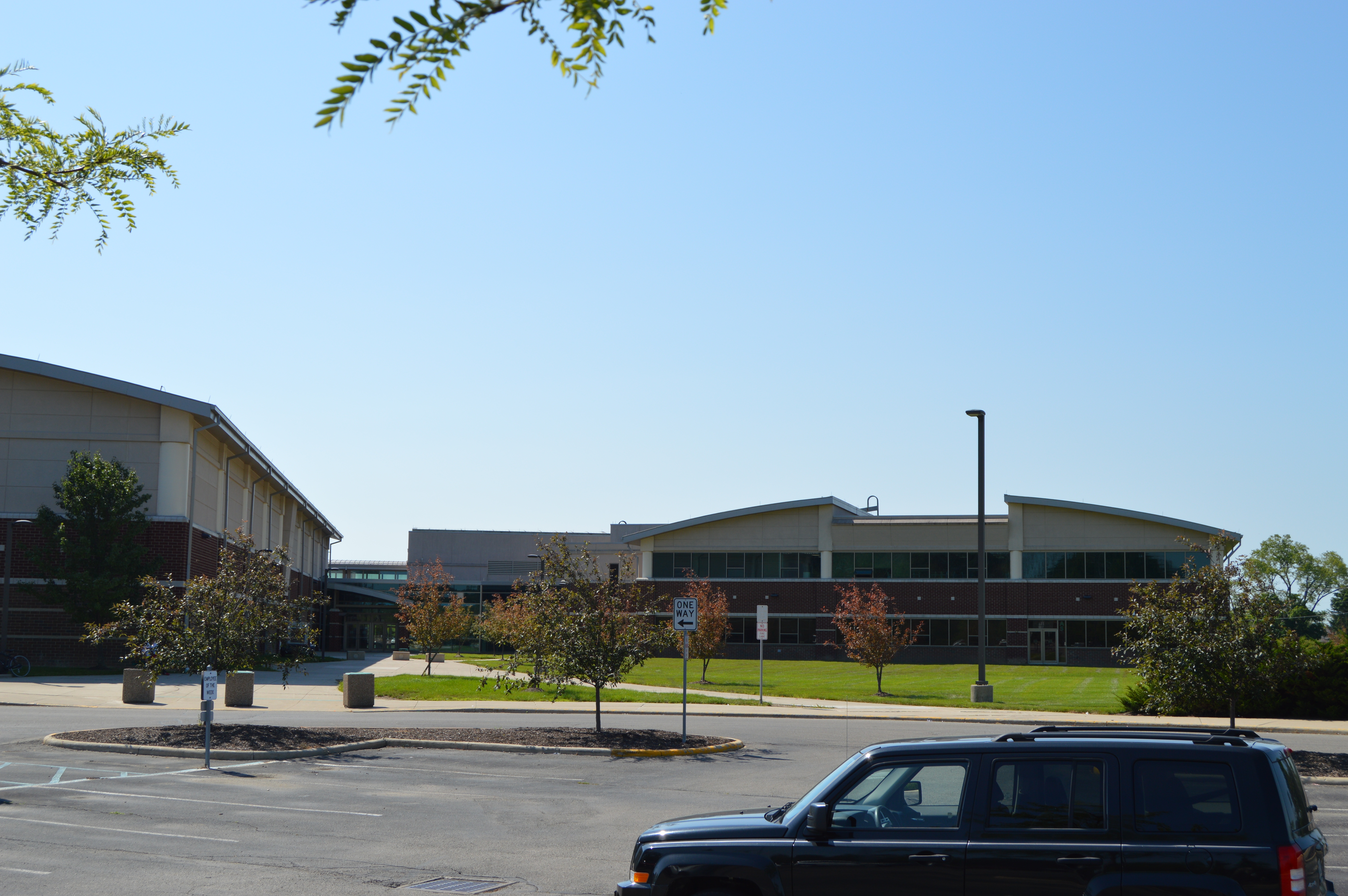 Large brick school building complex with parking lot under a clear blue sky.