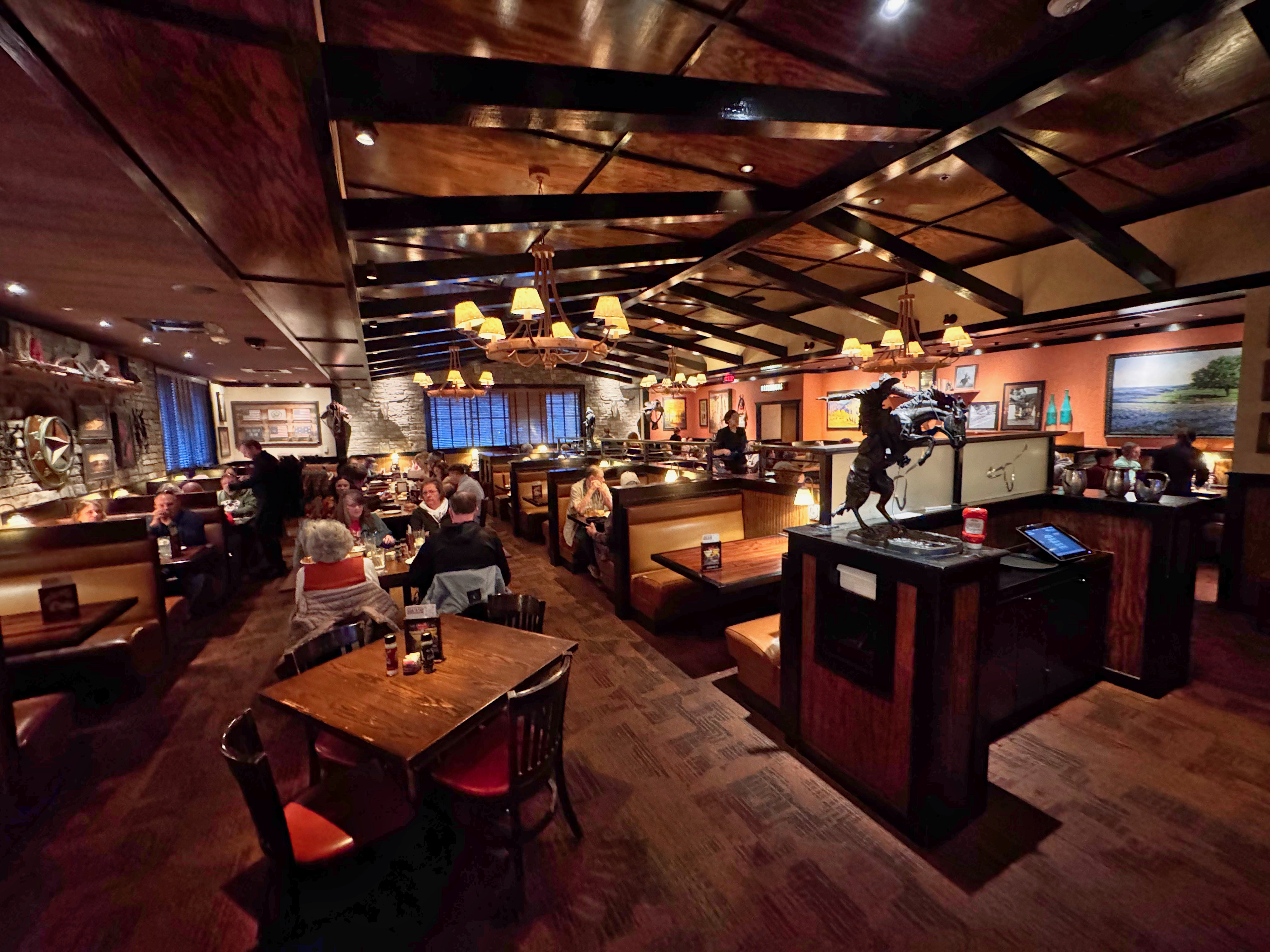 Steakhouse dining room interior with wooden booths and pendant chandeliers.