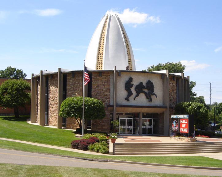 Stone exterior of the Pro Football Hall of Fame with a football-shaped dome and bronze player silhouettes.