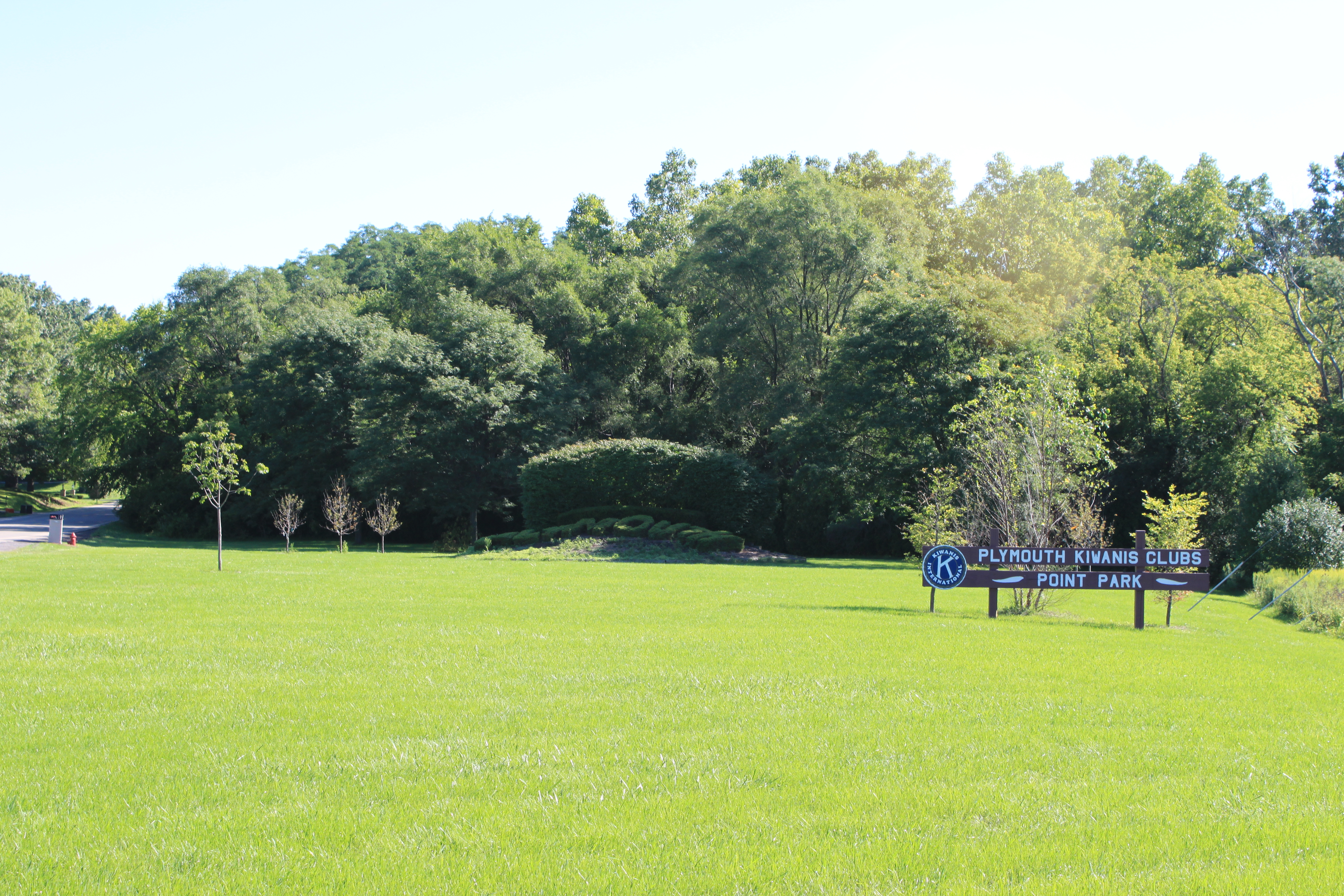 Open grassy park with a sign and mature trees under a blue sky.