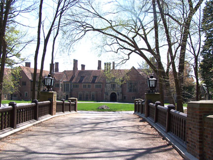 Brick Tudor mansion at the end of a tree-lined driveway with ornate gate pillars.