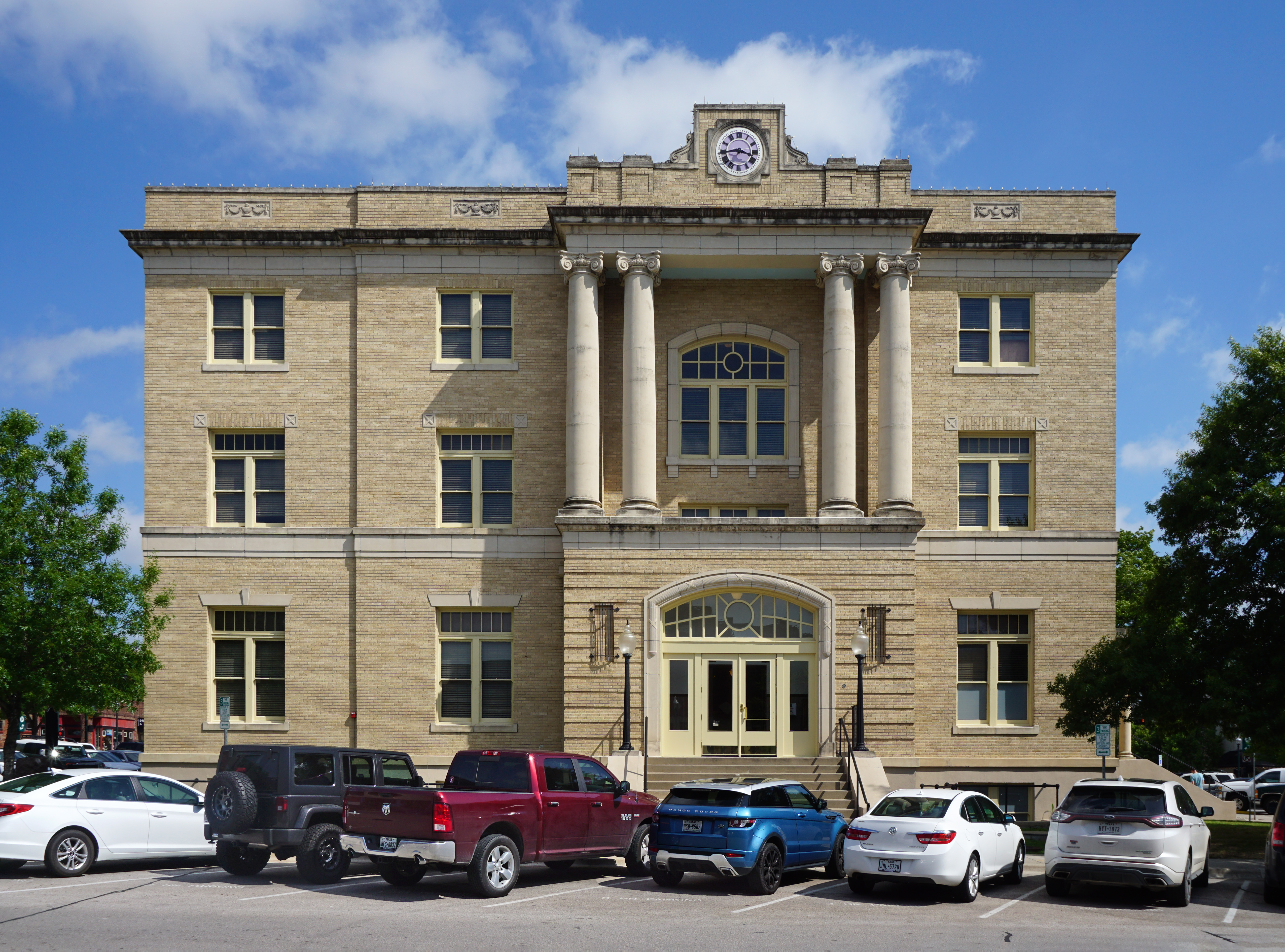 Three-story neoclassical limestone building with large columns and a clock near the roofline.
