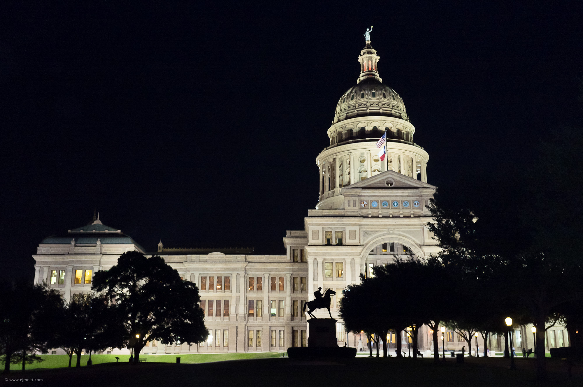 The Texas State Capitol building illuminated at night, with its dome and statue glowing against a dark sky.