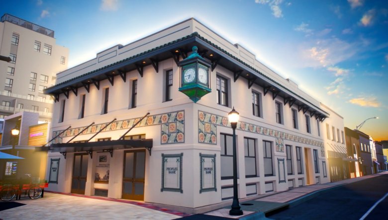 Two-story white Mediterranean Revival corner building with a four-faced green clock tower.