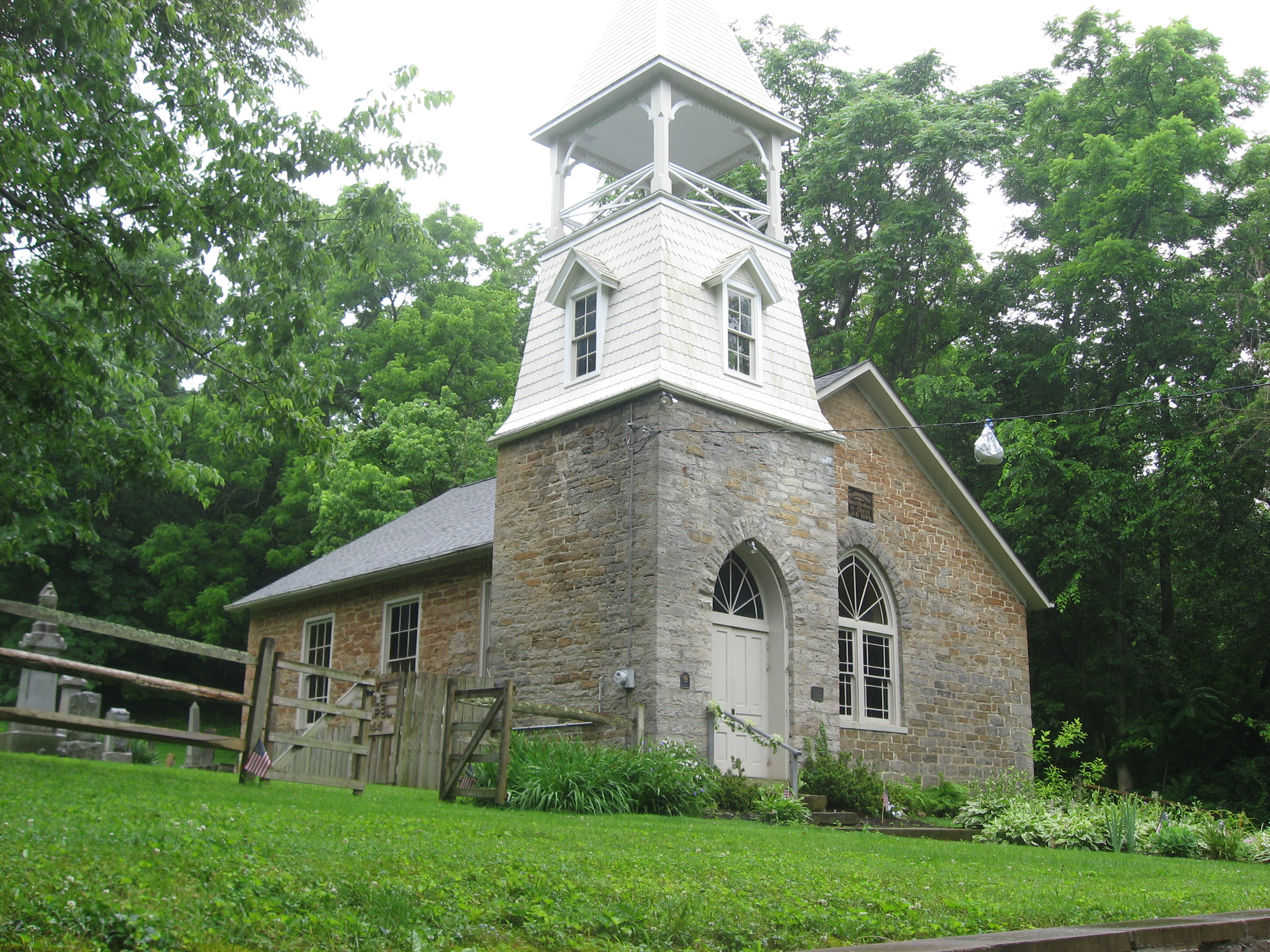 Historic stone church building with white bell tower and arched windows on a green lawn.