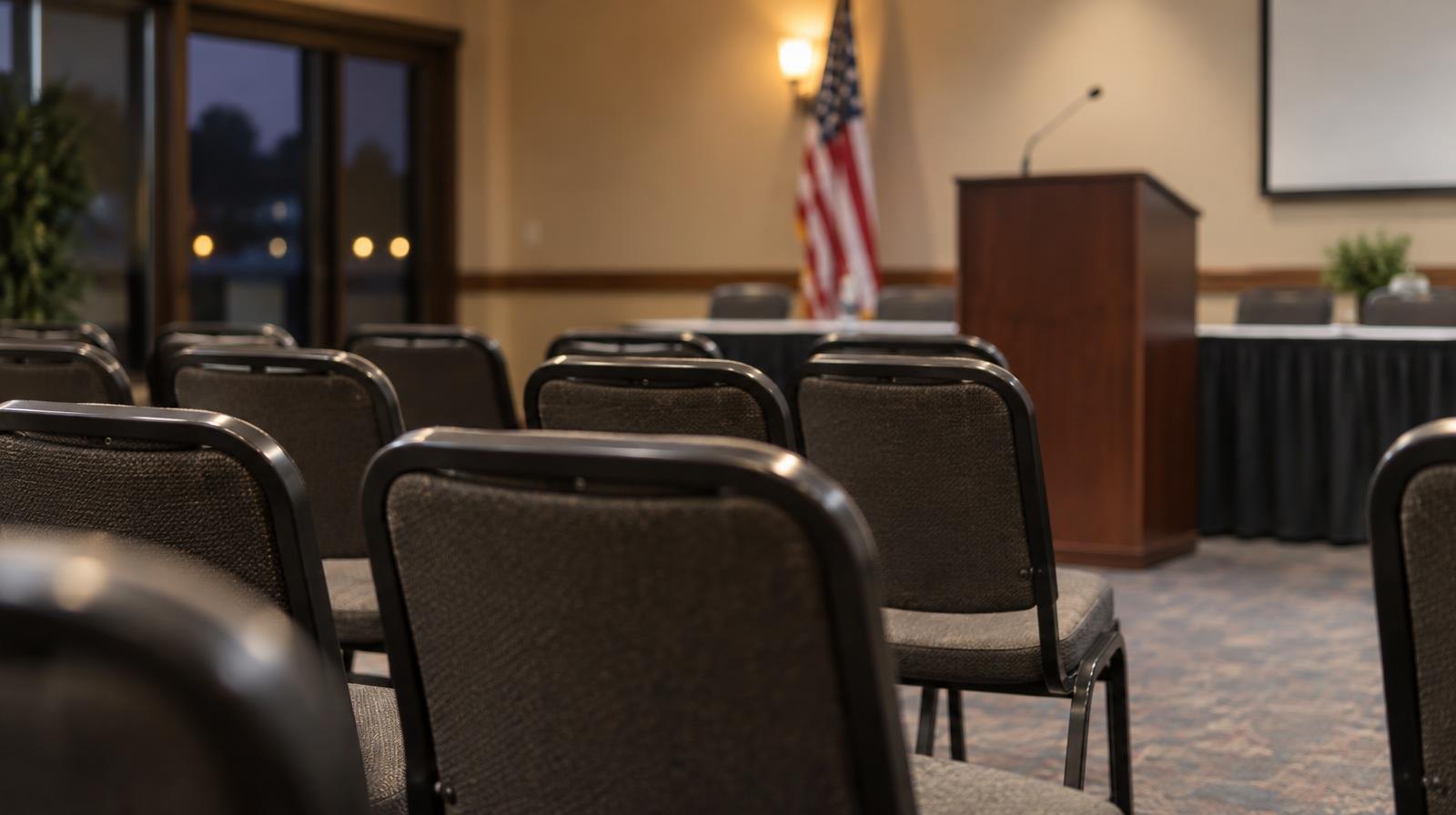 Rows of empty chairs face a podium in a warmly lit meeting room.