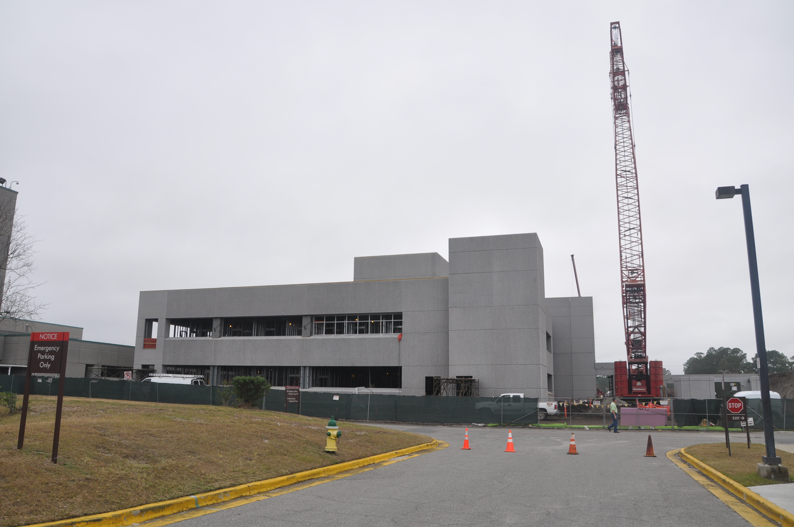 Gray hospital building under construction with a red crane and an emergency department entrance sign.