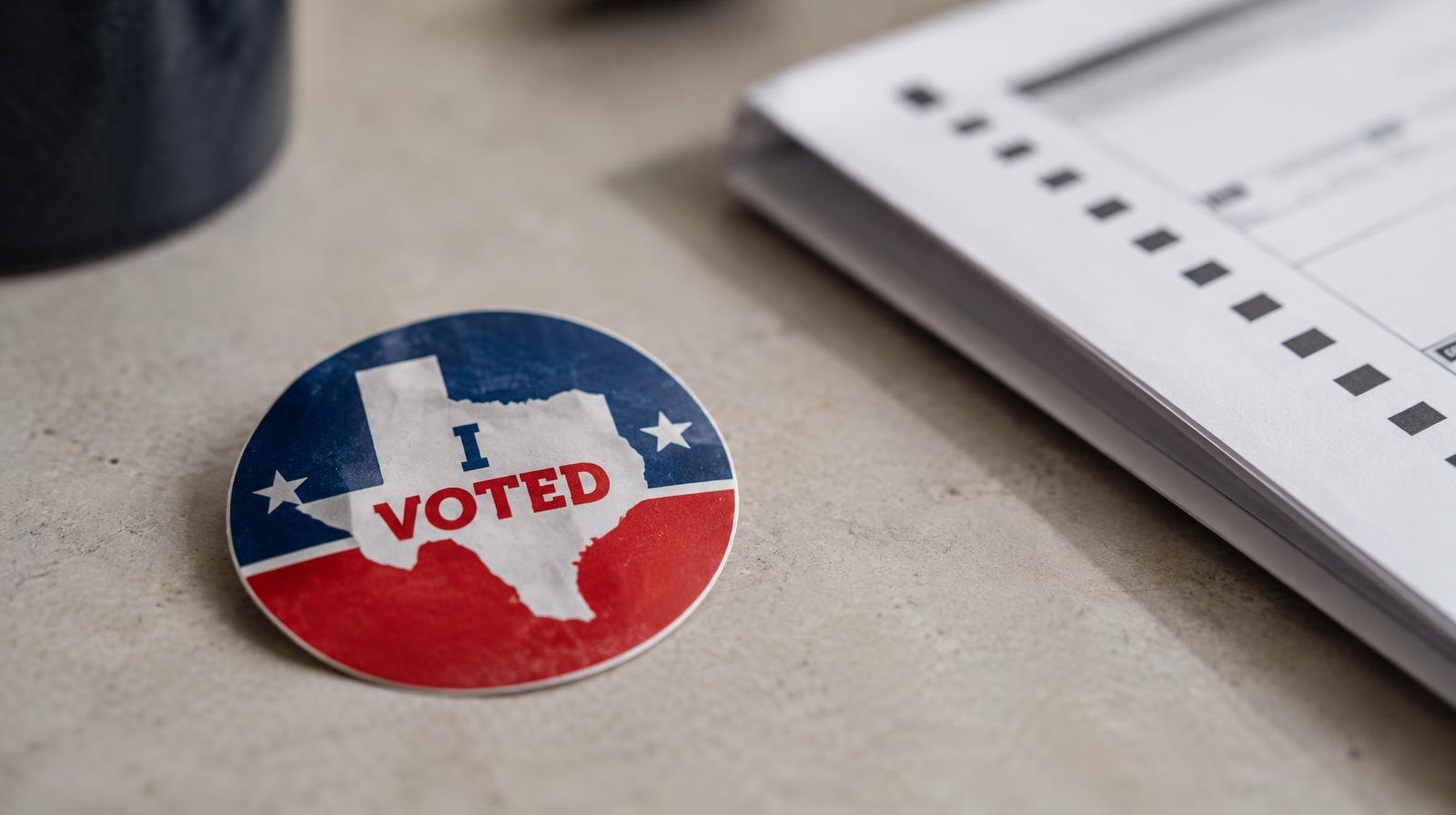 A Texas 'I Voted' sticker resting on a surface beside a folded paper ballot.
