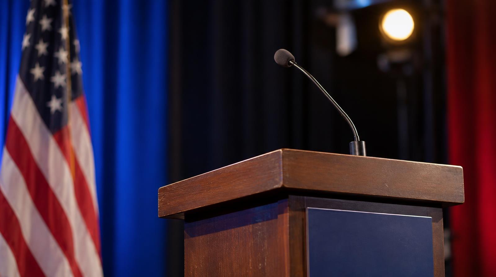 An empty podium with a microphone under bright stage lighting.