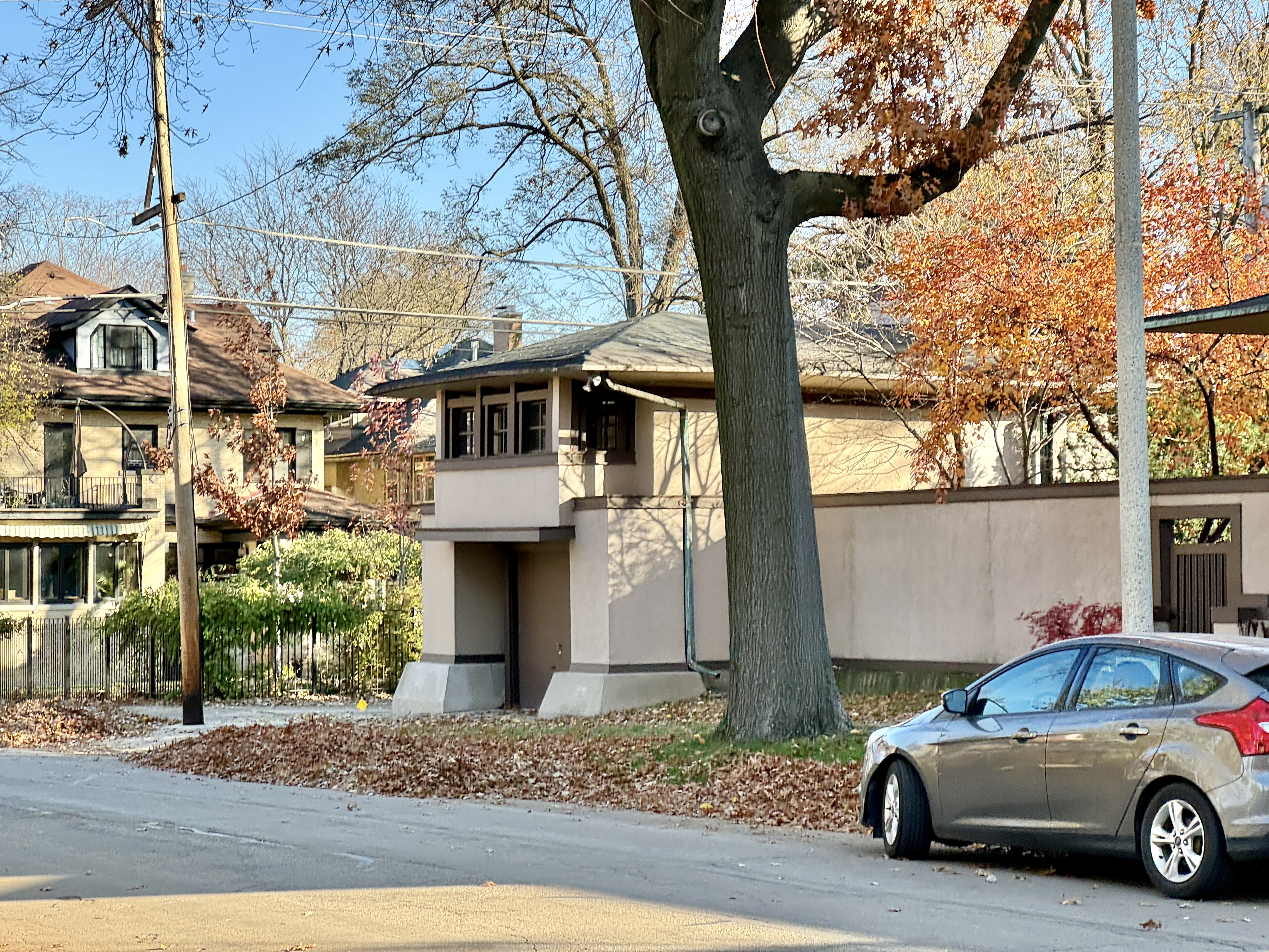 Two-story Prairie-style stucco house with autumn foliage and a car parked out front.