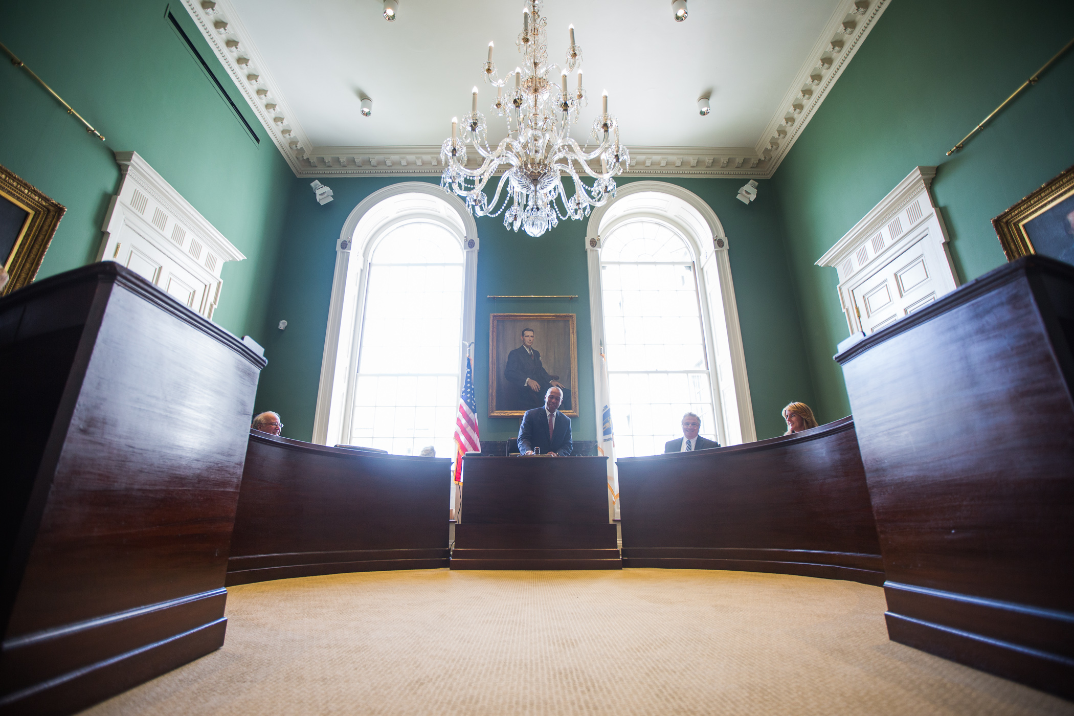 Officials seated at curved wooden desks in a formal government council chamber.