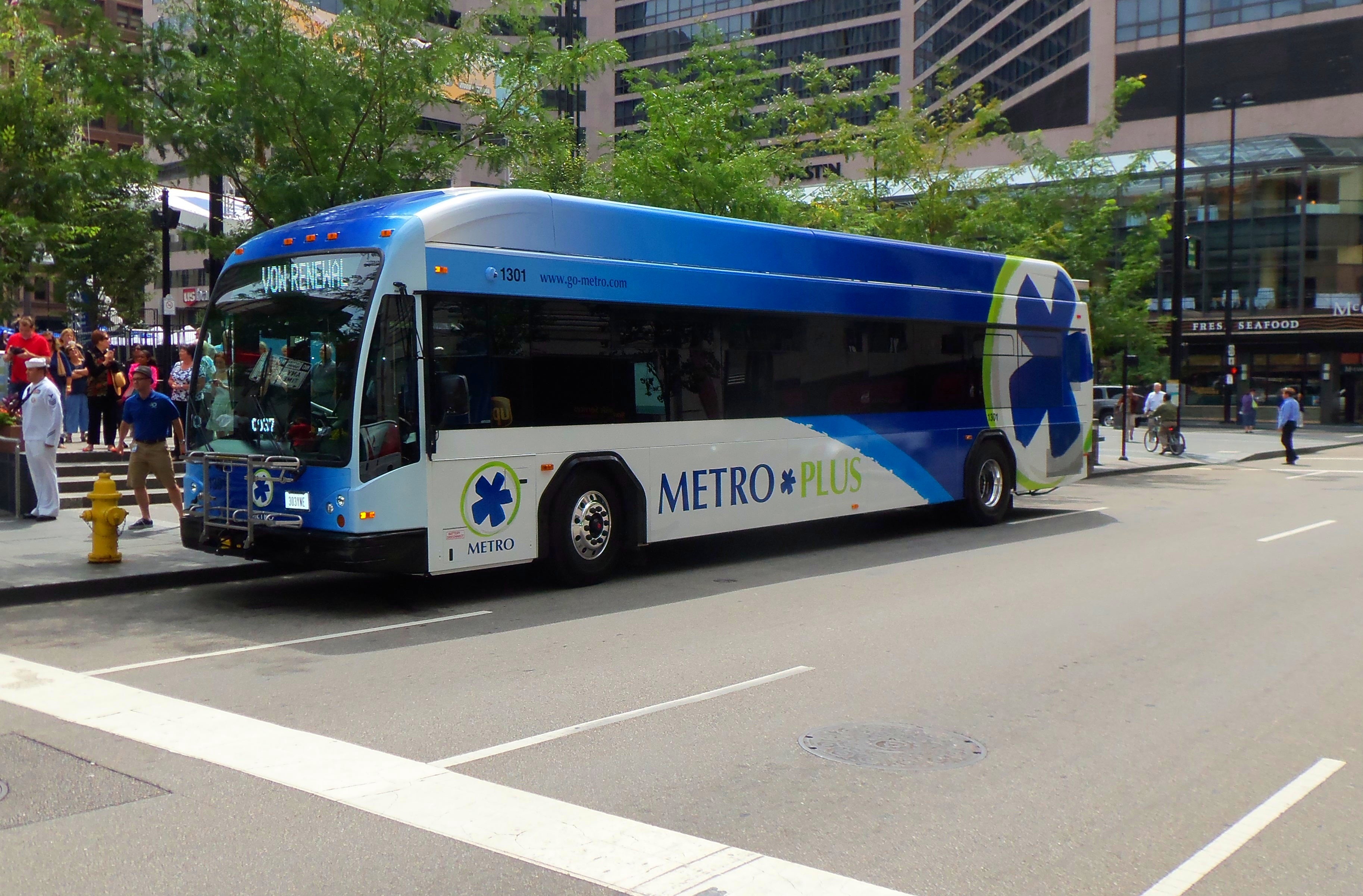 An articulated Metro Plus bus travels along an urban city street.