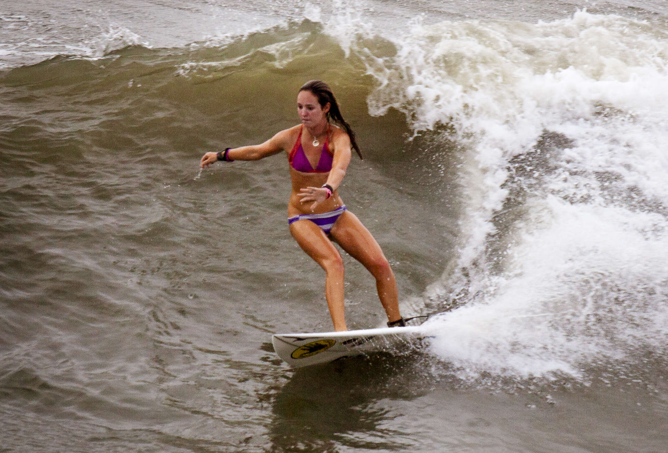 A woman in a purple bikini surfs a breaking wave on a white surfboard.