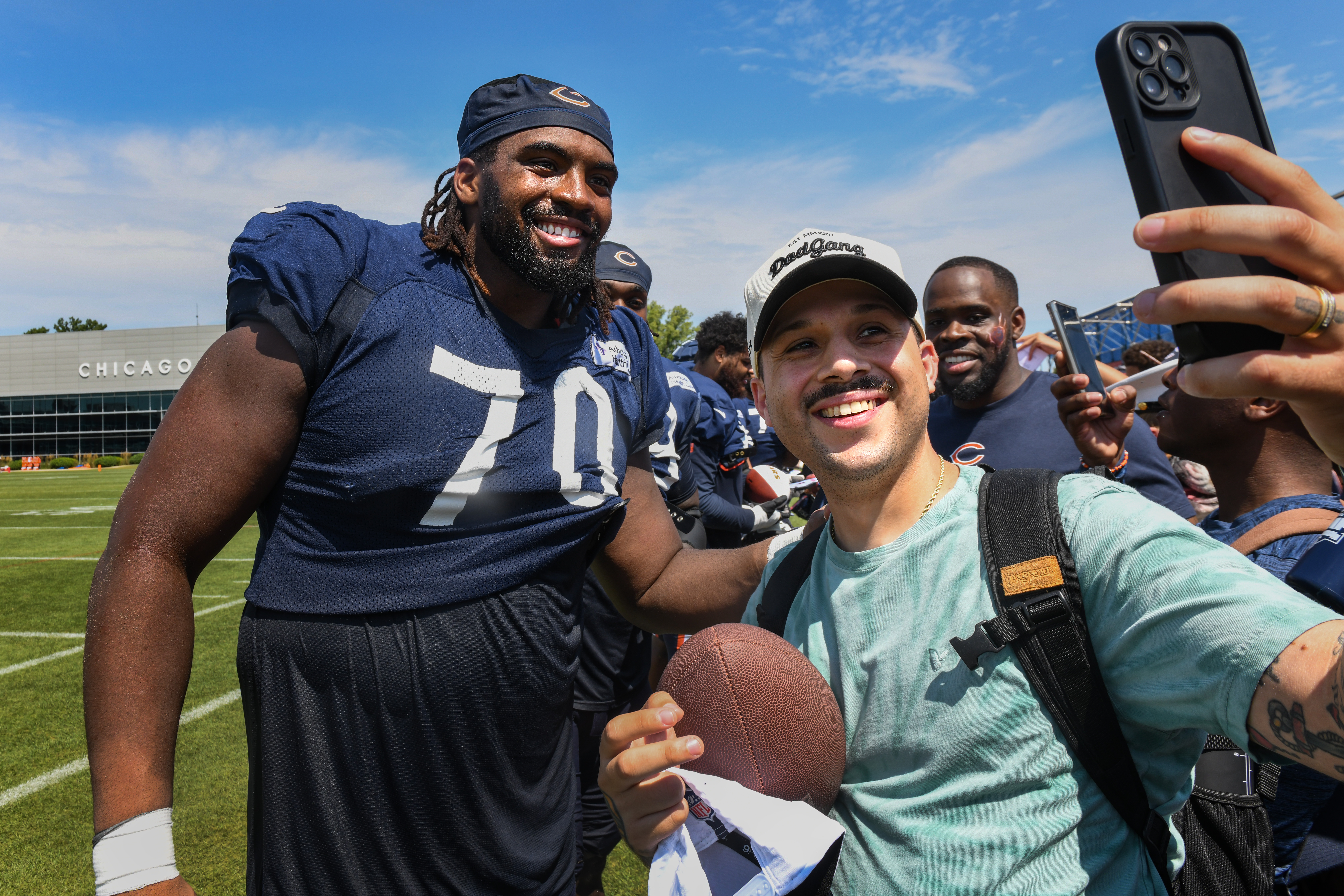 Chicago Bears player in jersey number 70 posing for a selfie with a fan on a practice field.