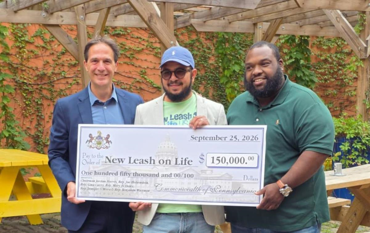 Three people stand outdoors holding a large ceremonial check for $150,000 made out to New Leash on Life.