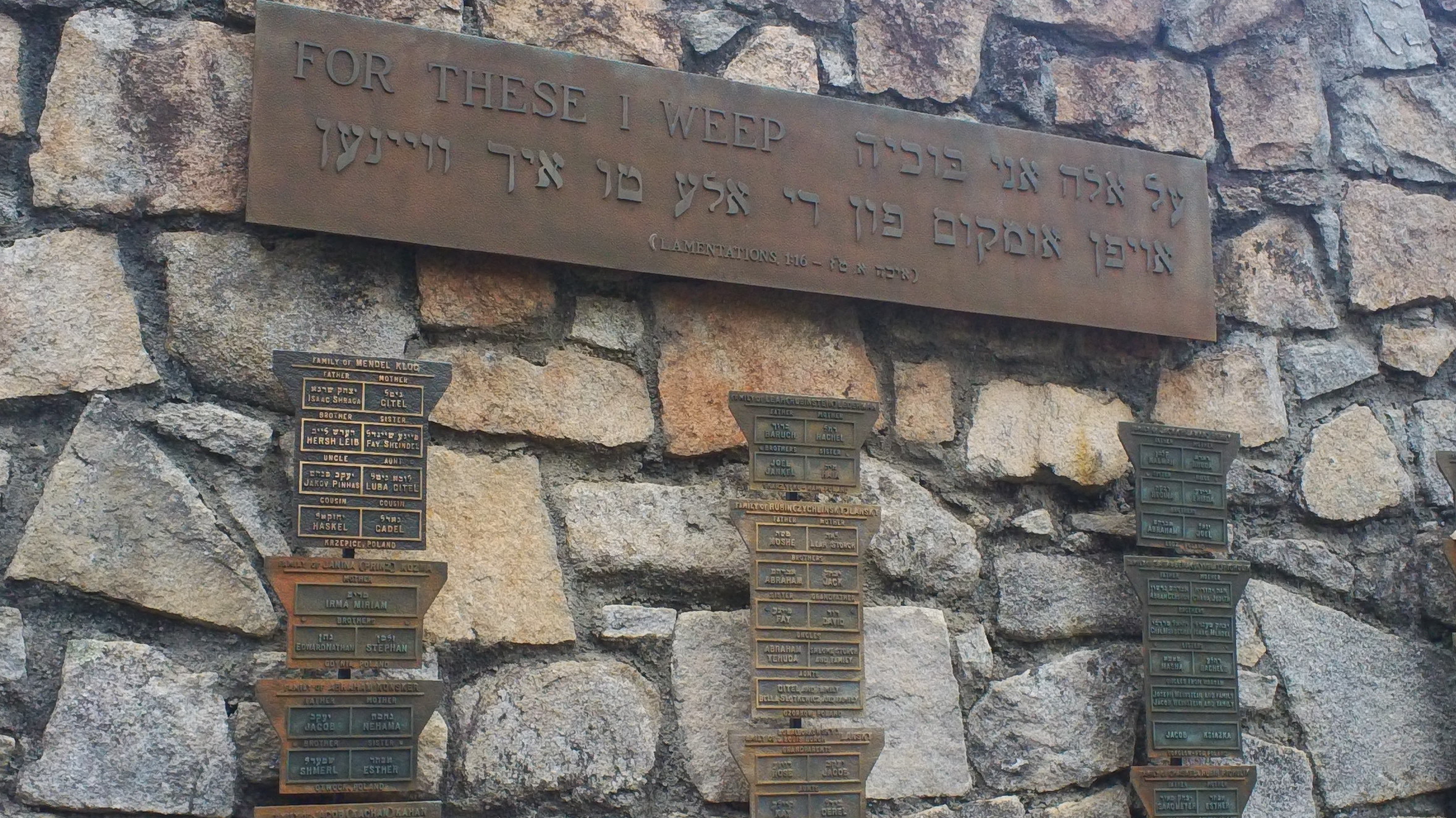 Stone memorial wall with bronze plaques inscribed in English, Hebrew, and Yiddish.